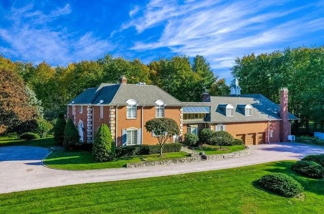 Large brick house with a curved driveway, surrounded by green lawn and trees, showing an ACES estate client's home.
