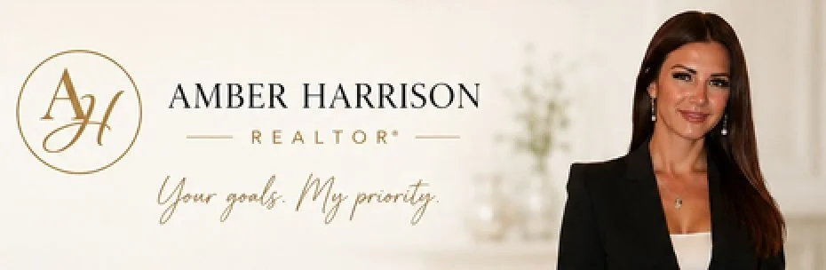 Business woman with long brown hair wearing a black blazer and white top, smiling, standing next to a sign for Amber Harrison, Realtor, with her logo and the tagline "Your goals. My priority."
