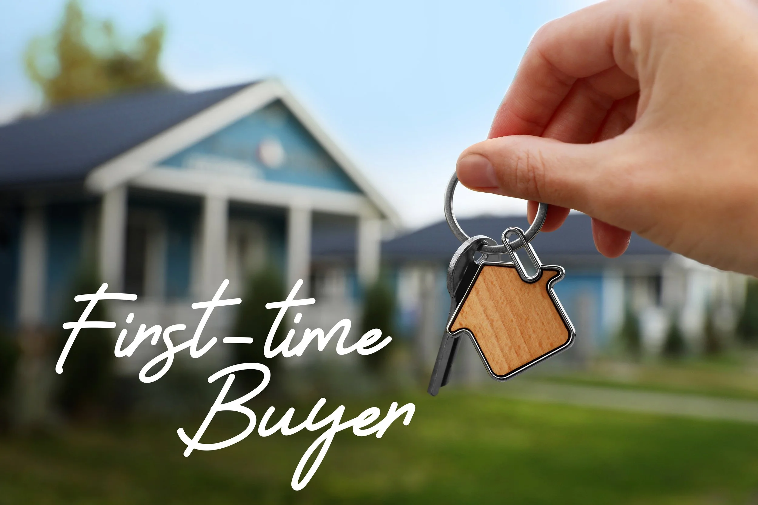 Close-up of a hand holding a keychain with a house-shaped pendant, with a blurred house in the background and the text 'First-time Buyer' in white cursive.