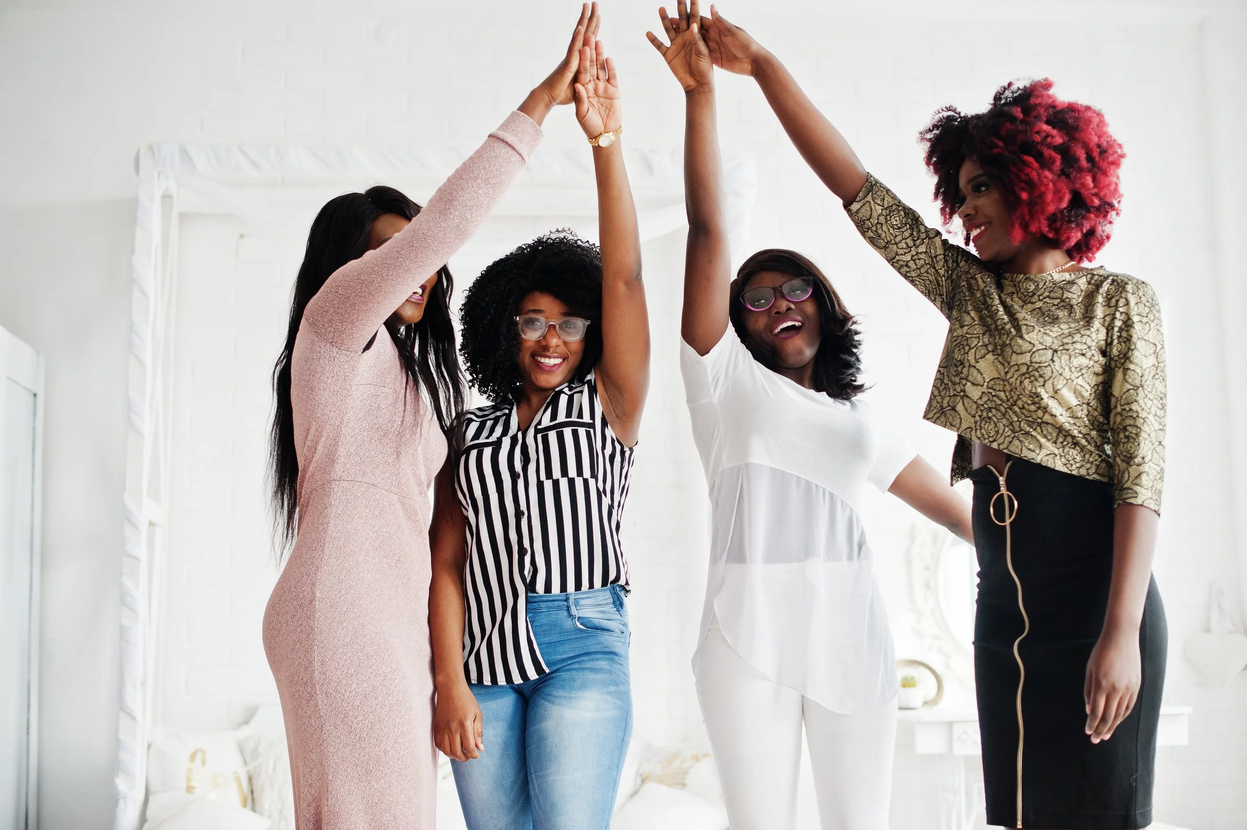 Four diverse women smiling and giving high five in a bright room.