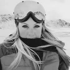 A woman wearing a helmet and goggles, smiling in a snowy outdoor landscape.