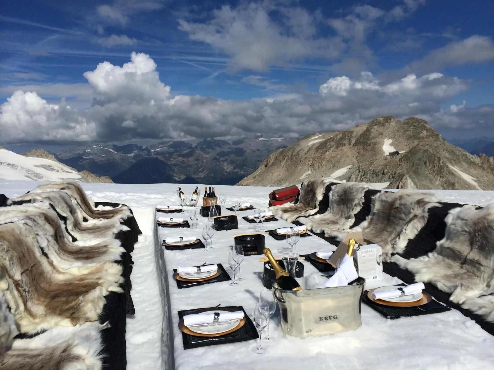 A mountain landscape with snow-capped peaks, a grassy hillside, and a modern building in the foreground.