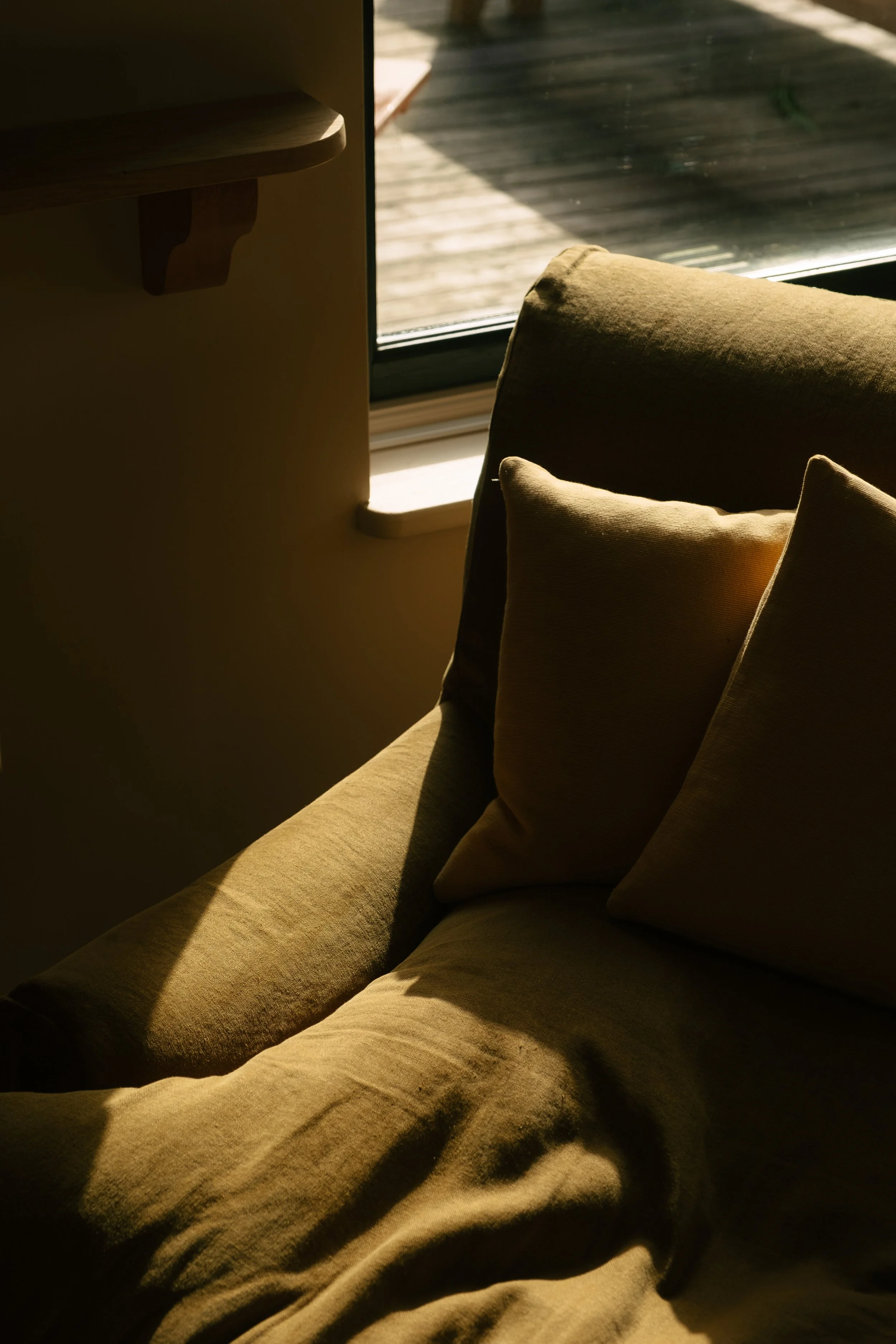 A beige sofa with cushions near a window with sunlight streaming in