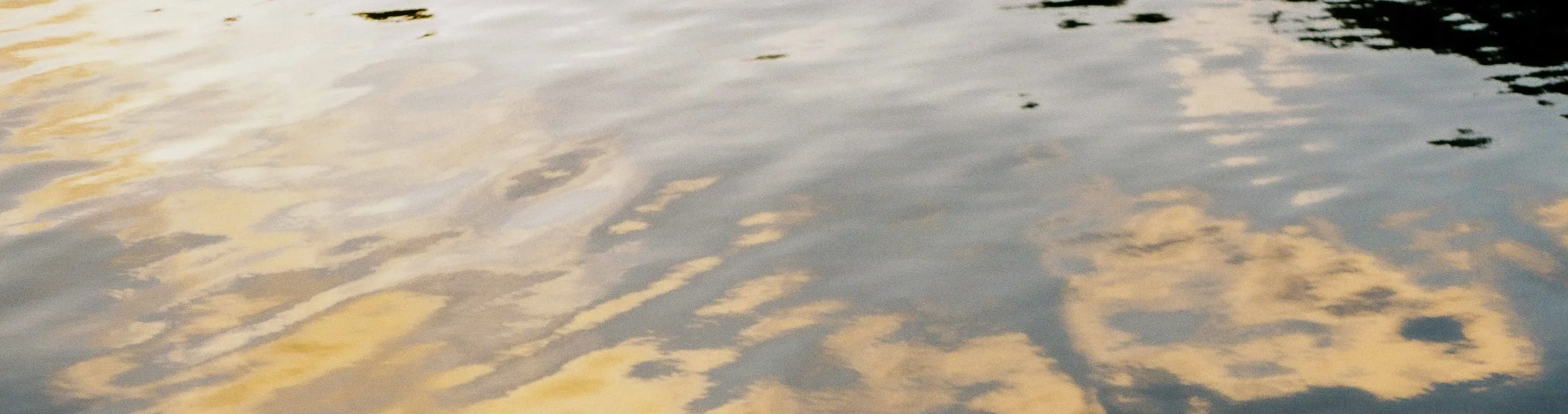 Reflection of clouds on calm water surface during sunset or sunrise.