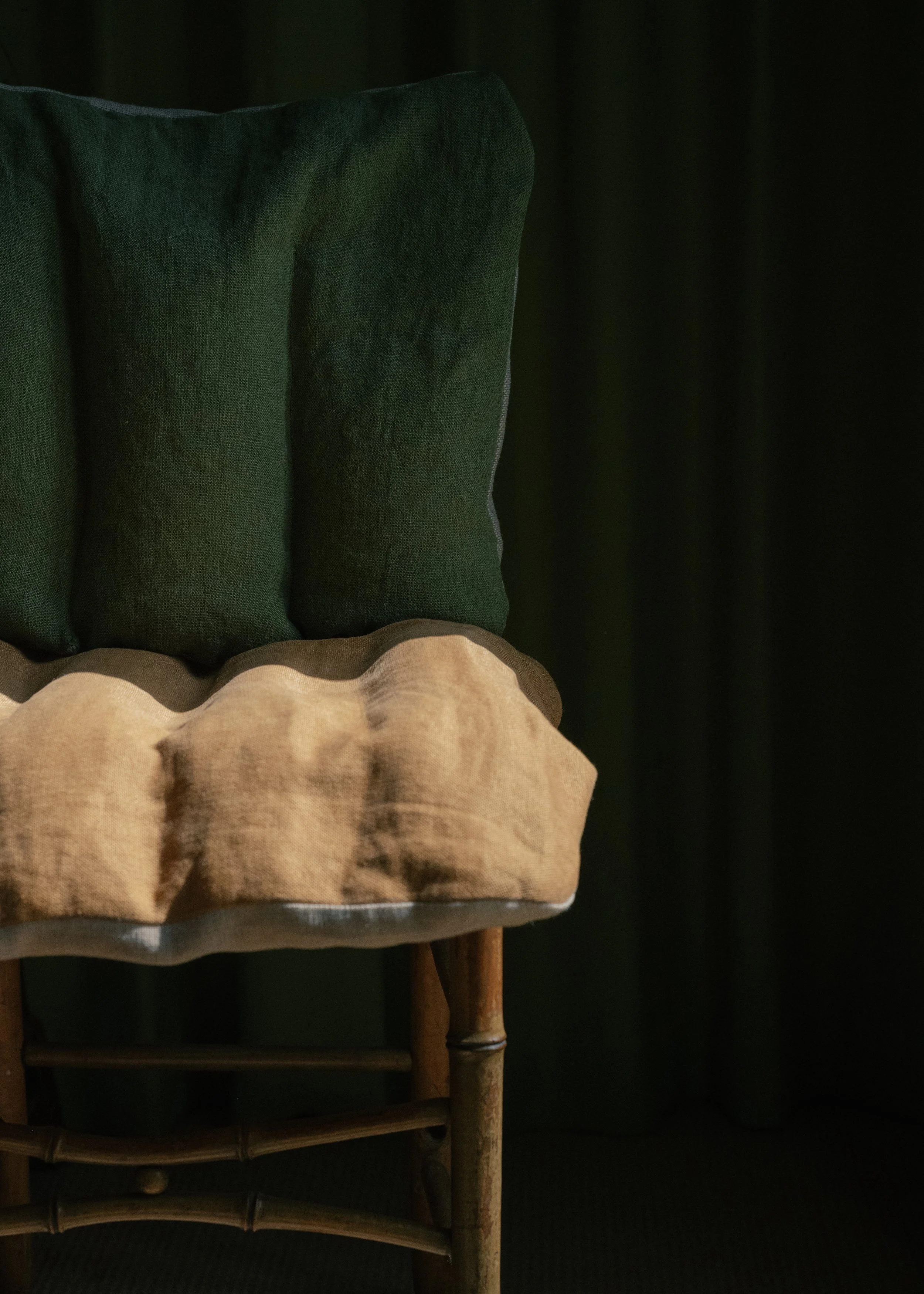 Part of a bed with a wooden frame and two pillows, one beige with a ruffled edge and the other dark green, against a black background.