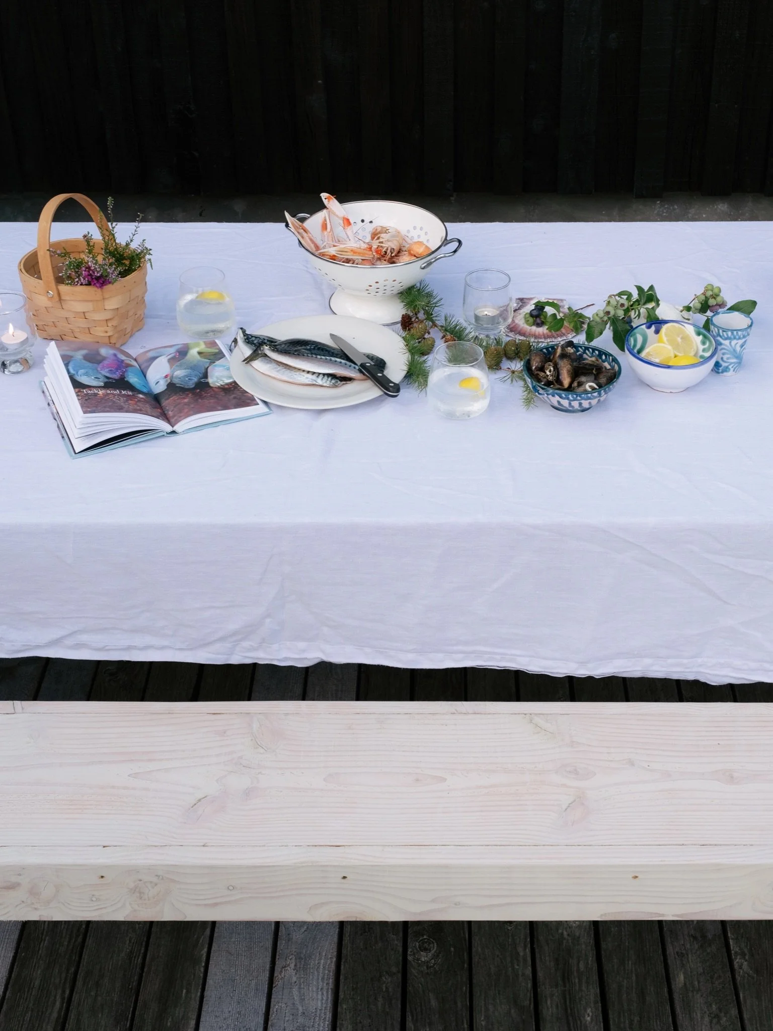 Table set outdoors with seafood dishes, glasses, a book, and decorative elements on a white tablecloth.