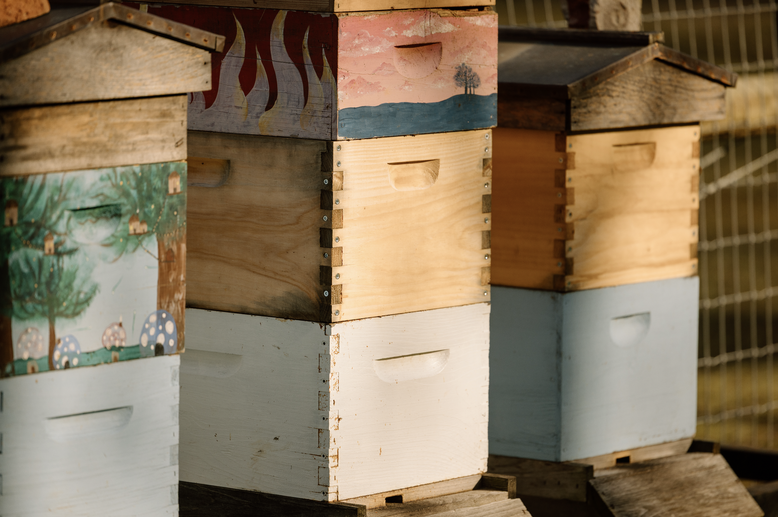 Multiple colorful wooden bee hives with painted designs, stacked on a wooden platform outside.