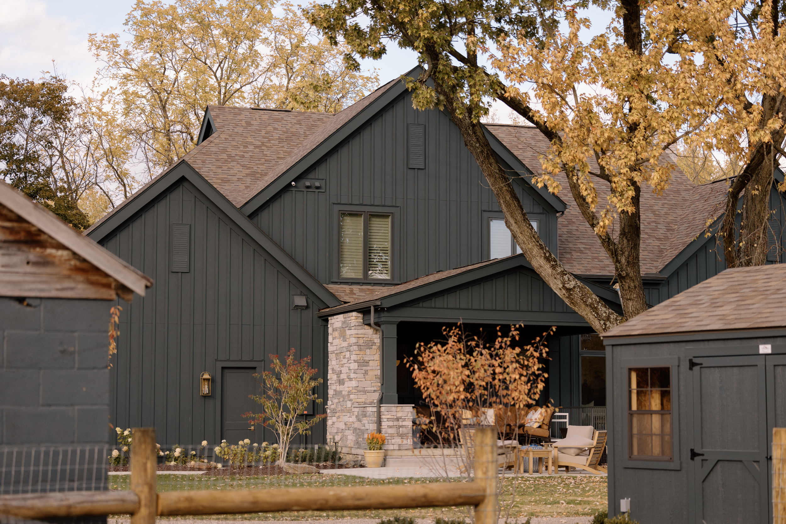 A modern dark blue house with a gabled roof and stone accents, surrounded by autumn trees and outdoor seating at Nature's Curve Farm