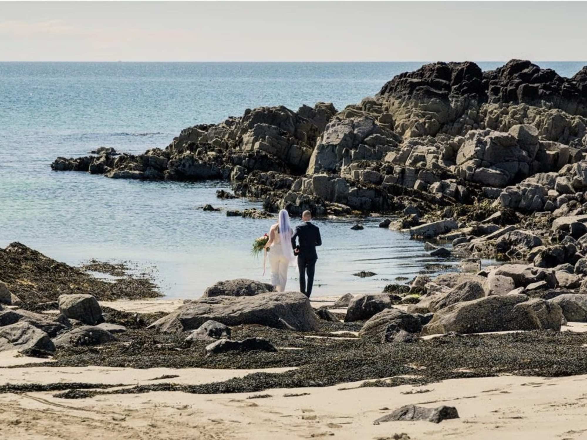 Brautpaar von hinten an der schottischen Küste, Klippen im Hintergrund, Braut mit Strauß in der Hand