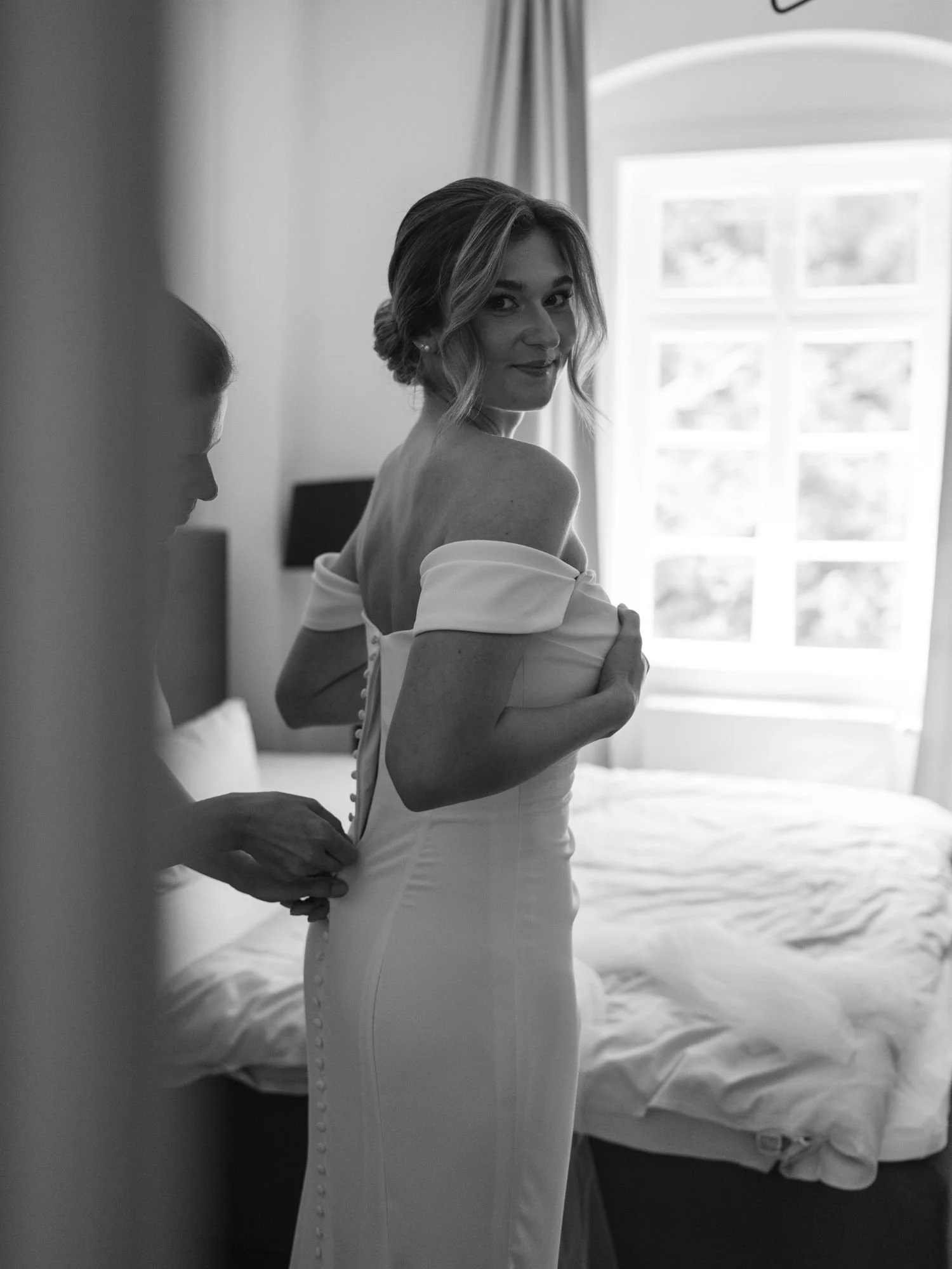 Braut beim Schließen ihres Kleides mit Unterstützung einer zweiten Person.