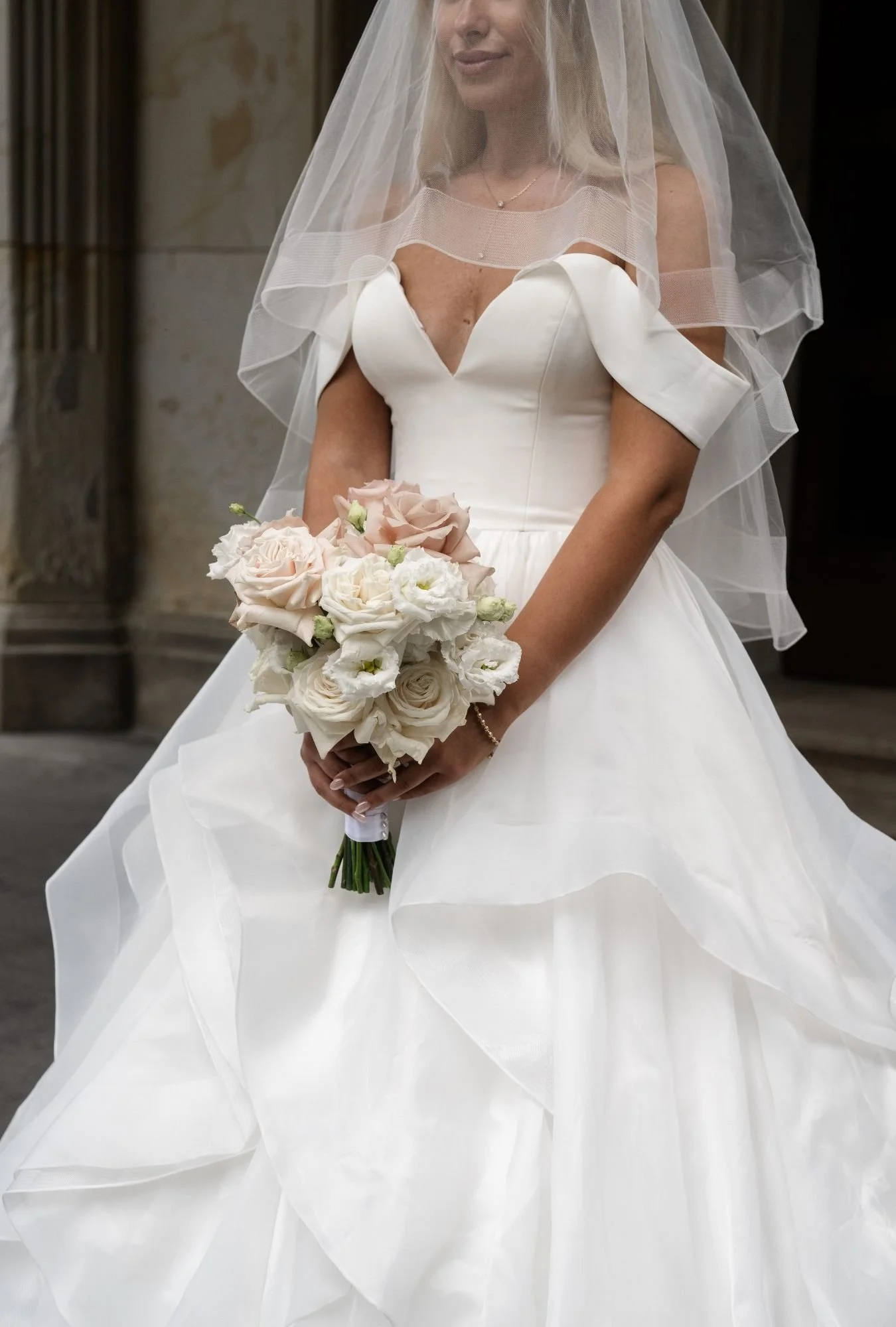 Braut mit Schleier hält ihren Brautstrauß im natürlichen Licht