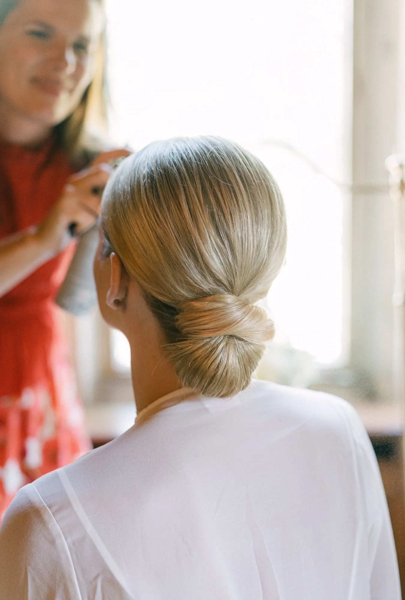 Detailaufnahme von Brautfrisur mit modernem Sleek Look und Brautstylistin im Hintergrund