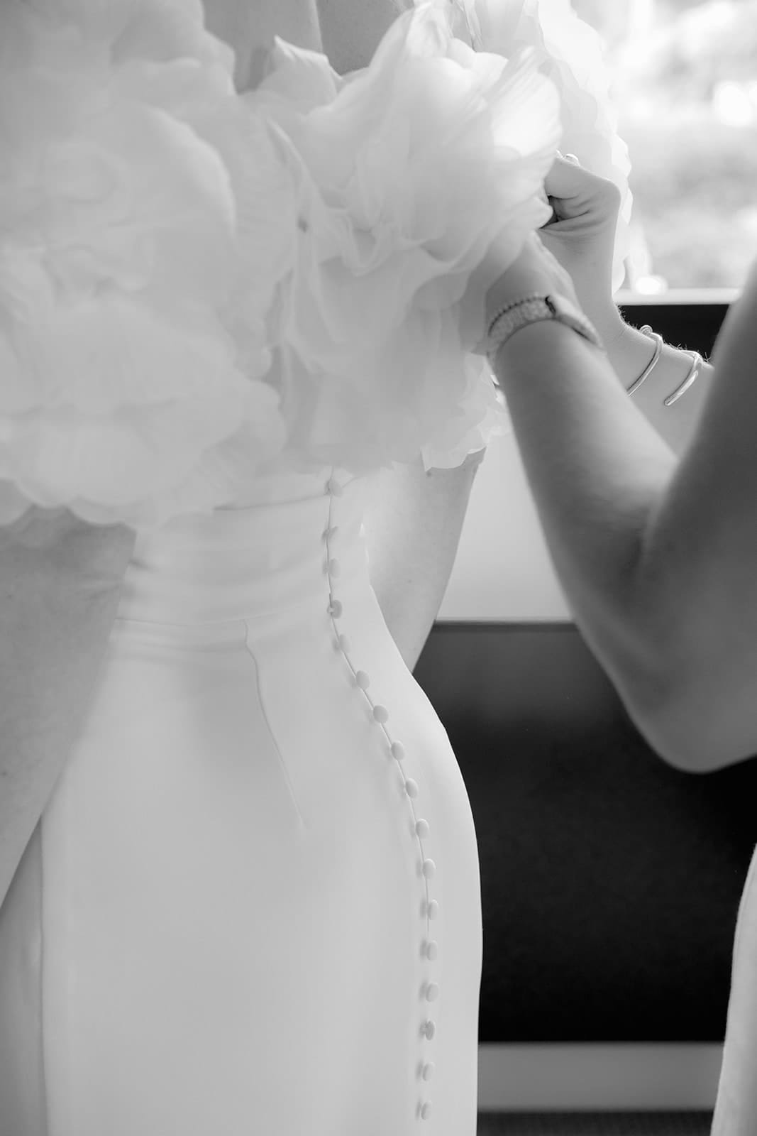 Hände knöpfen ein modernes Brautkleid zu