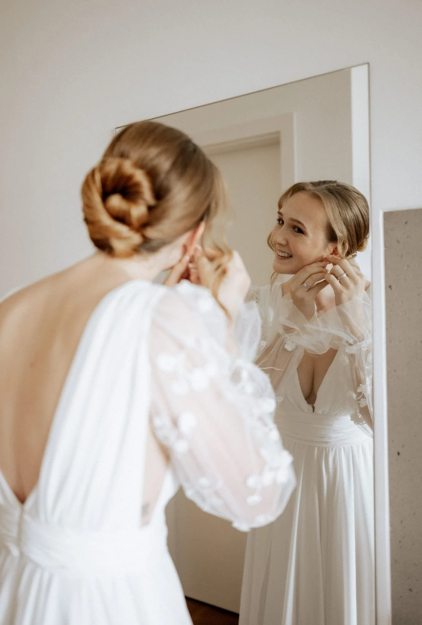 Braut mit einer eleganten Hochsteckfrisur mit modernem Finish beim Anlegen der Ohrringe