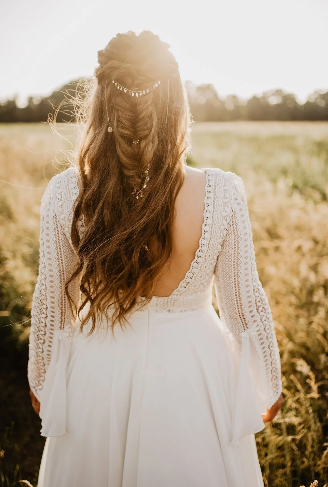 Elegante Aufnahme der Braut mit Boho Hairstyling auf Wiese in Abendsonne
