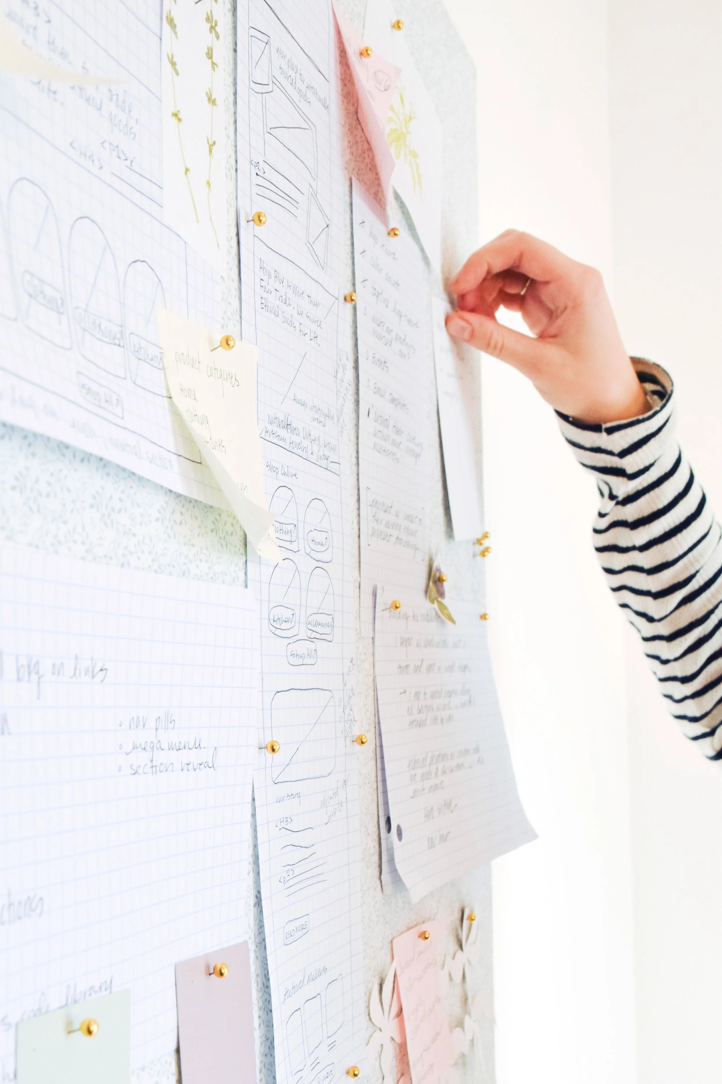 Person pinning papers on a white bulletin board with various notes and sketches.