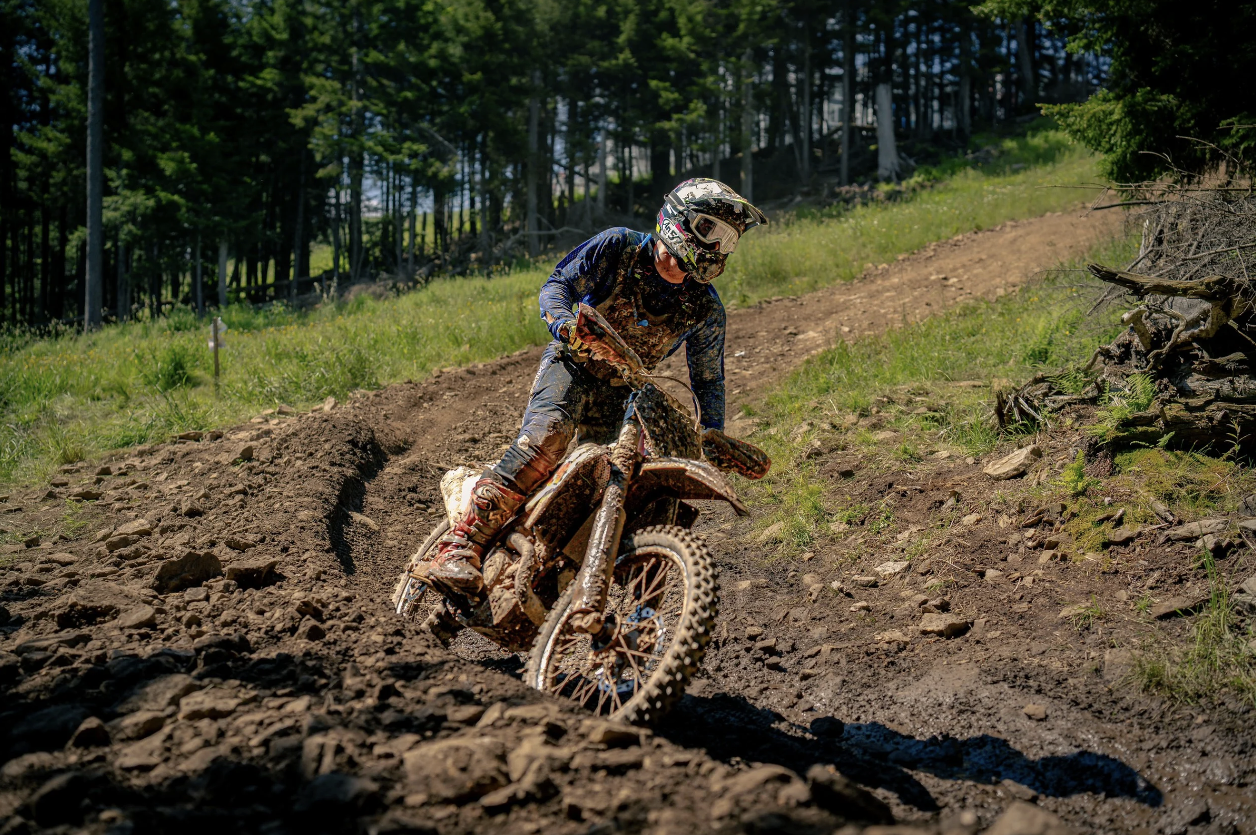 A person riding a dirt bike on a muddy trail in a forested area.