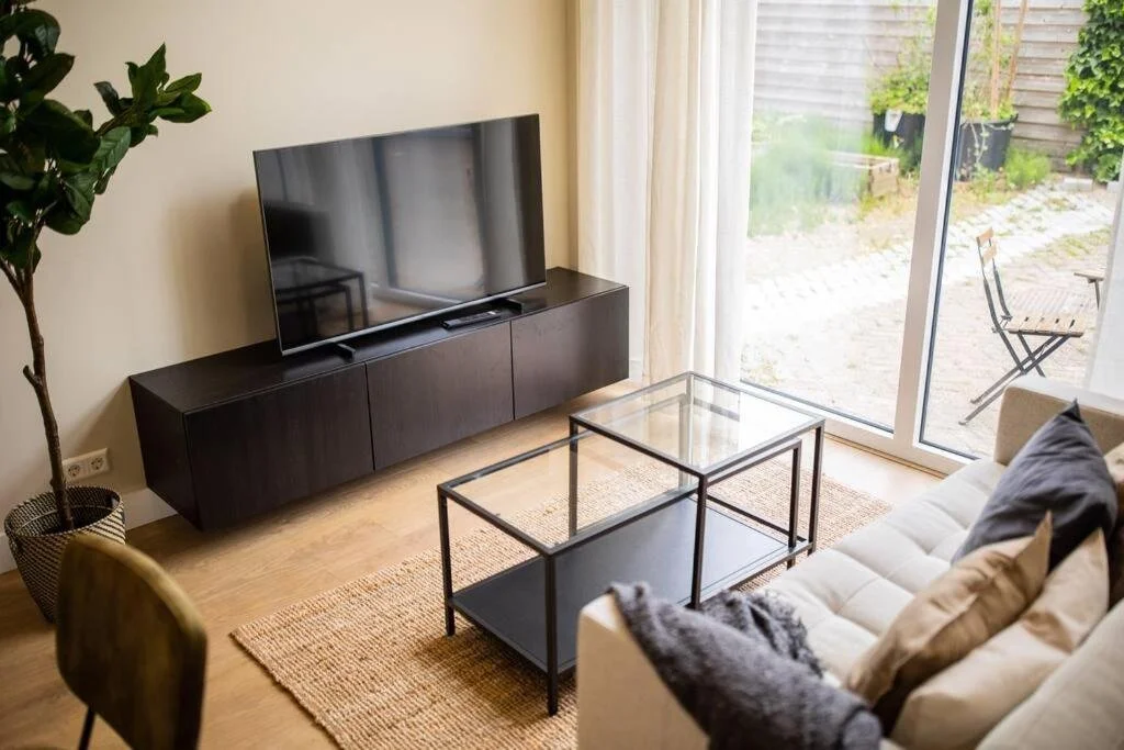 Woonkamer met TV, bank, glazen salontafel en grote glazen deur naar tuin