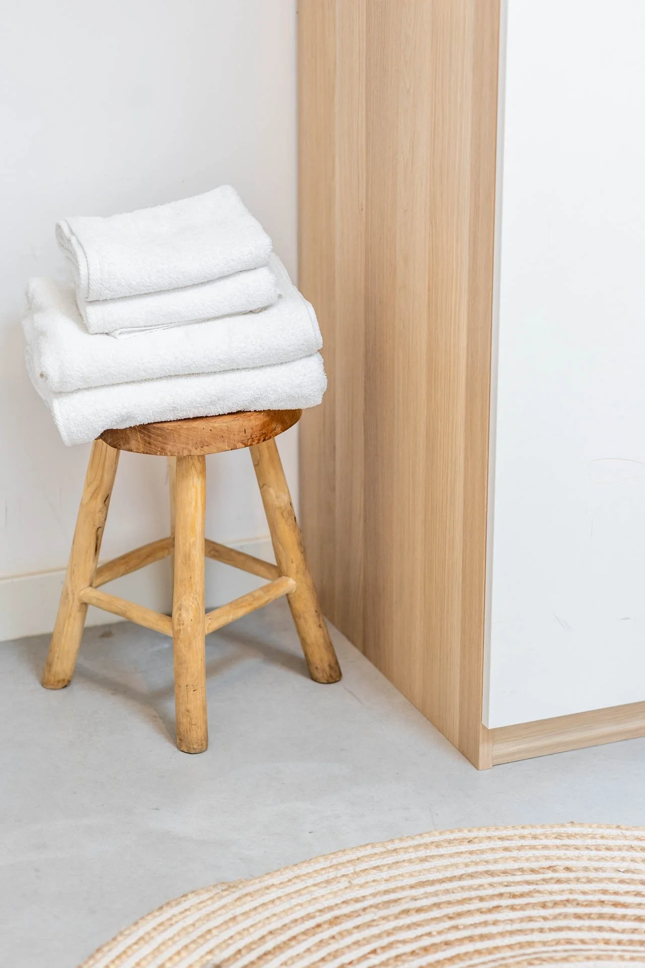 Gedeclongeerde witte handdoeken op een houten kruk naast een meubelstuk met een lichte houtafwerking.