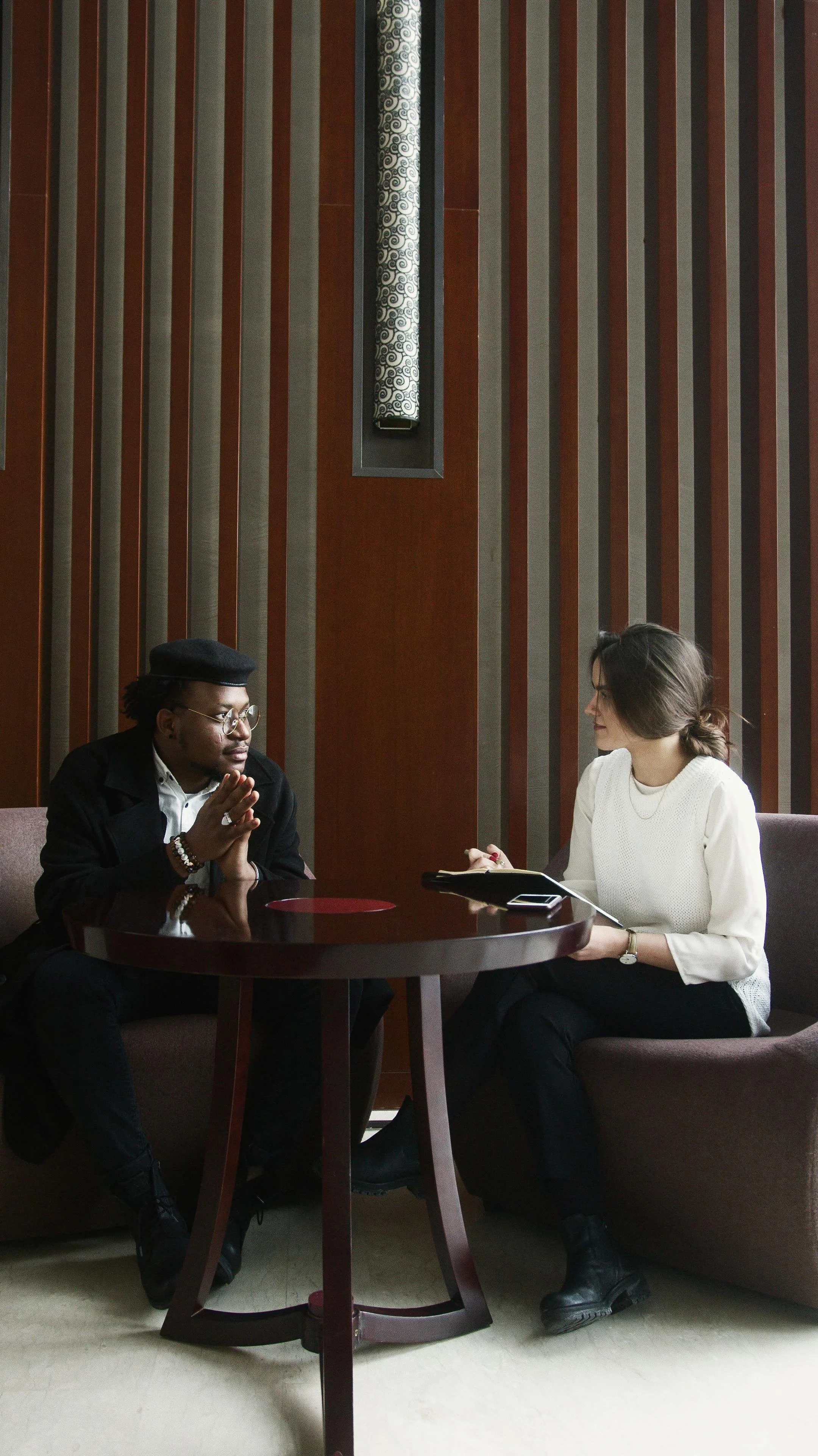 Two women sitting at a round table engaged in conversation in a modern indoor setting.