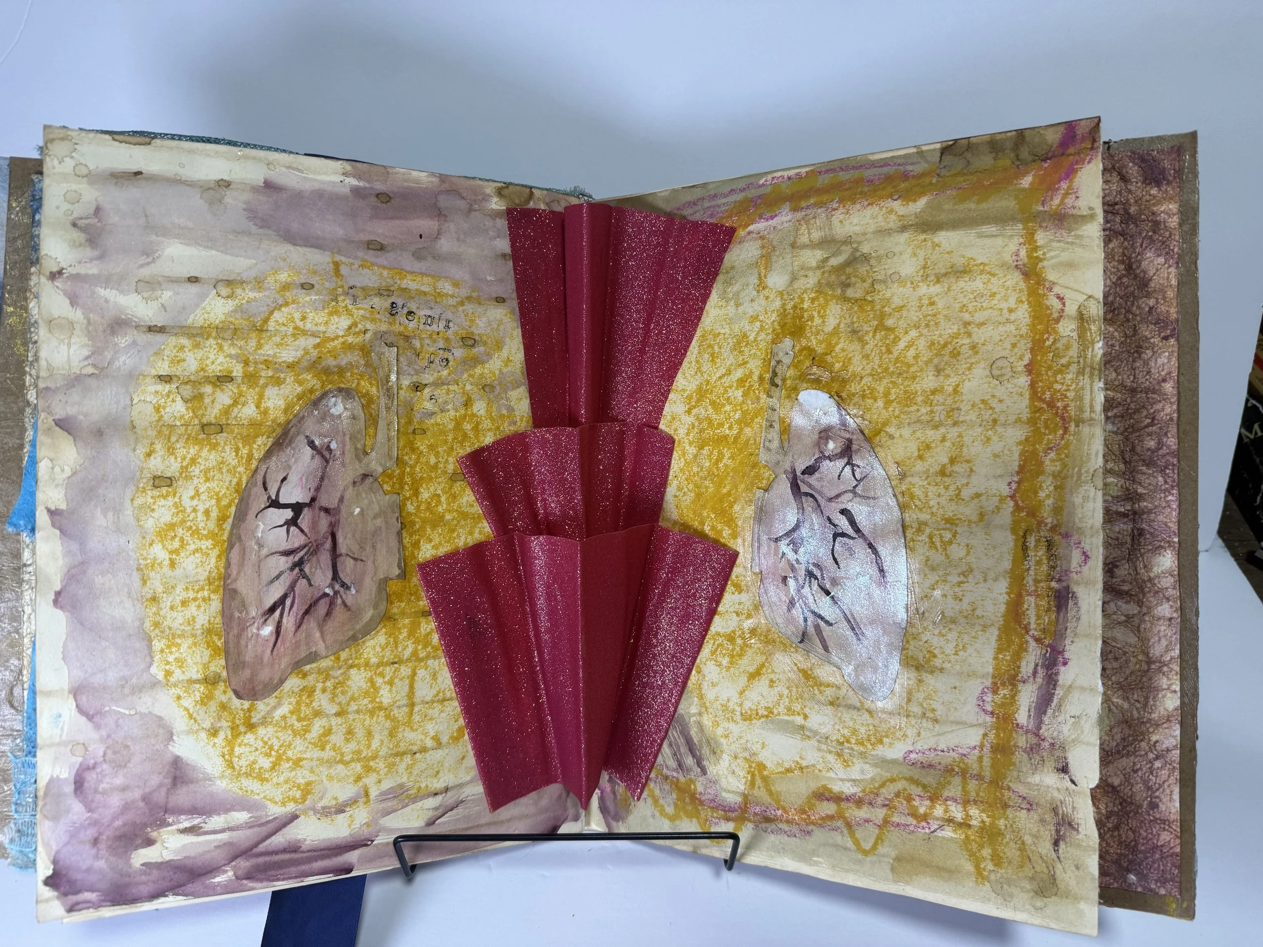 An art journal opened to pages painted with watercolor and marker, featuring abstract brain illustrations with black branching lines, highlighted with yellow, purple, and pink accents, and flanked by three-dimensional red paper embellishments in the center.