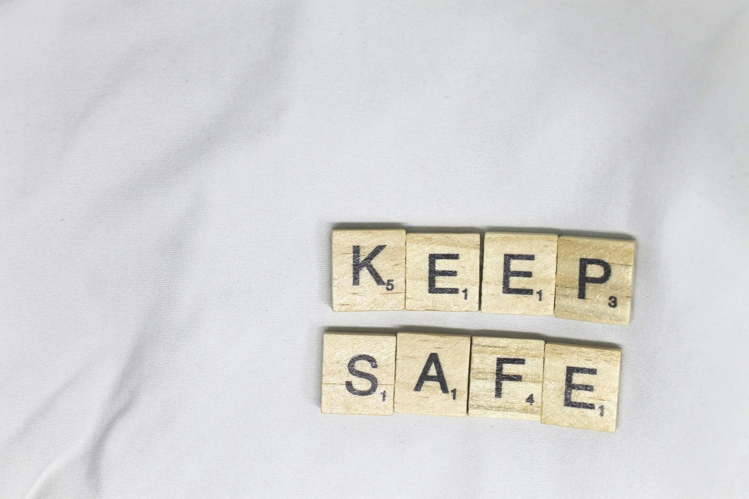 Scrabble tiles spelling out 'KEEP SAFE' on white fabric.