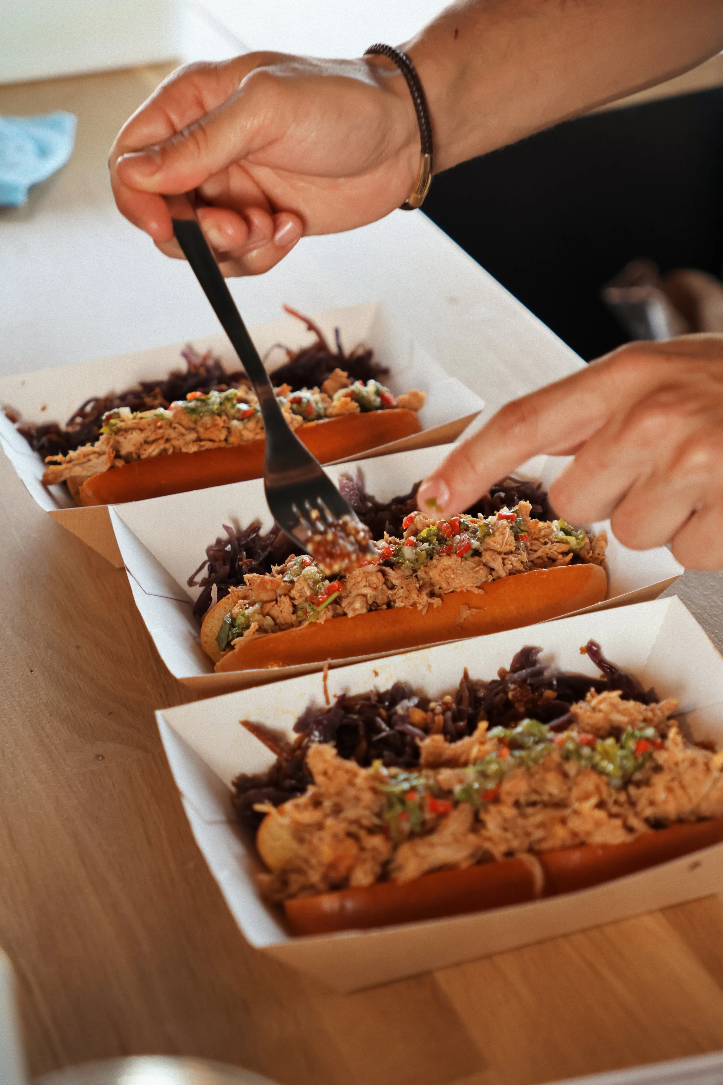 Personne déguste des tacos garnis de viande, légumes et salsa, dans des boîtes en carton sur une table en bois.