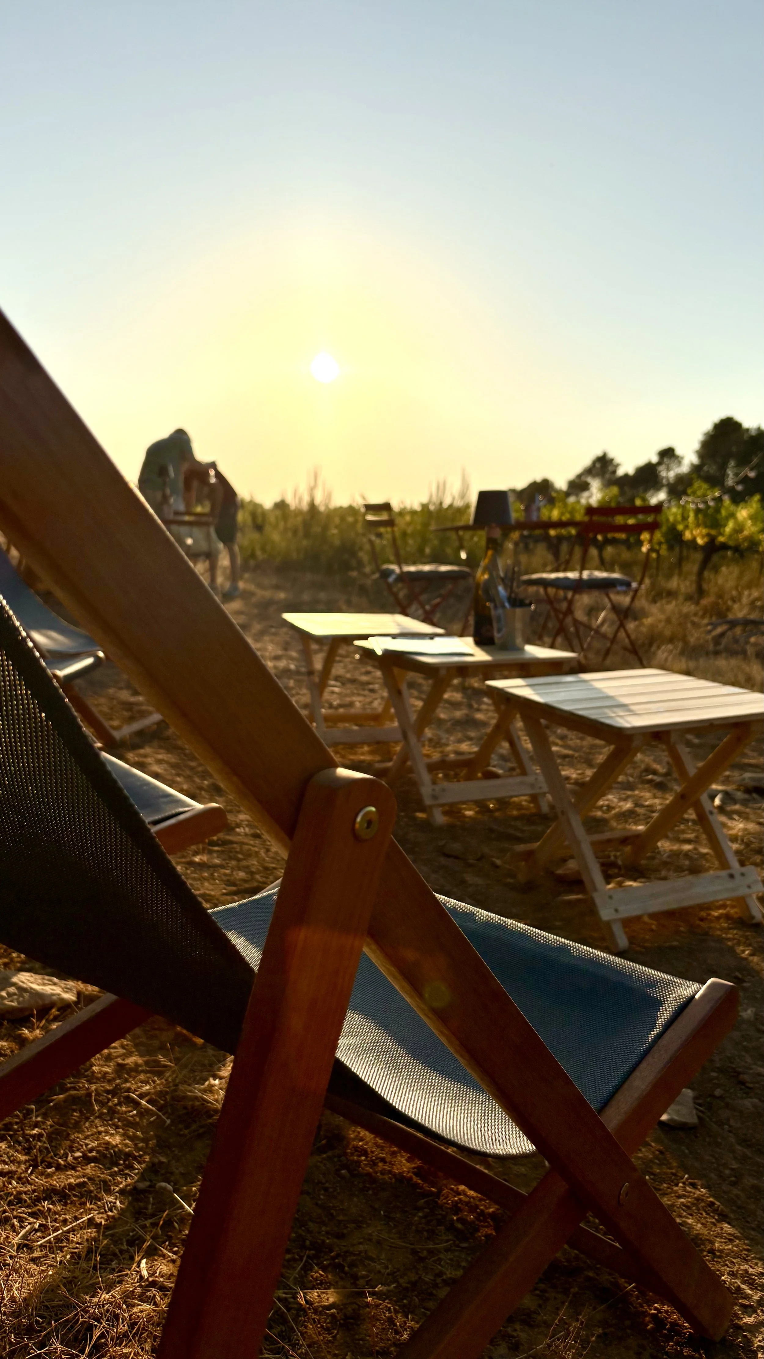 Chaises et tables en bois sur un terrain avec le soleil couchant.