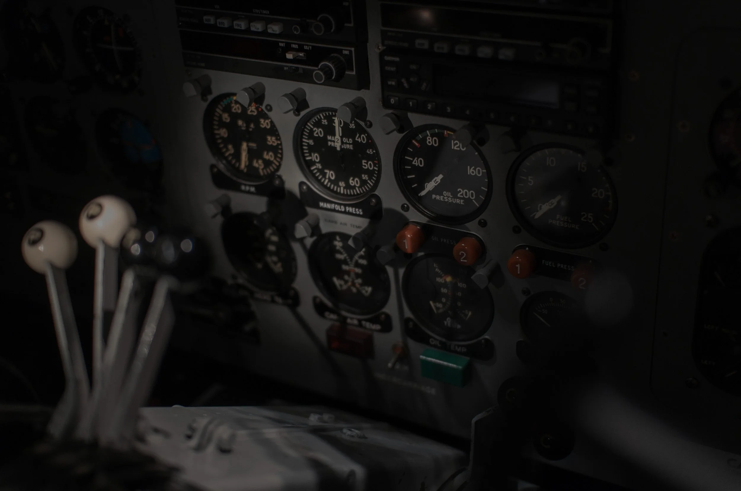 Close-up of an airplane cockpit instrument panel with various gauges, knobs, and switches, seen in low light.