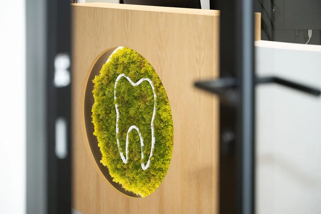 Het logo van Mondzorg Voorne als muurdecoratie met de omtrek van een tand omringd door groen mos in de praktijk in Hellevoetsluis.