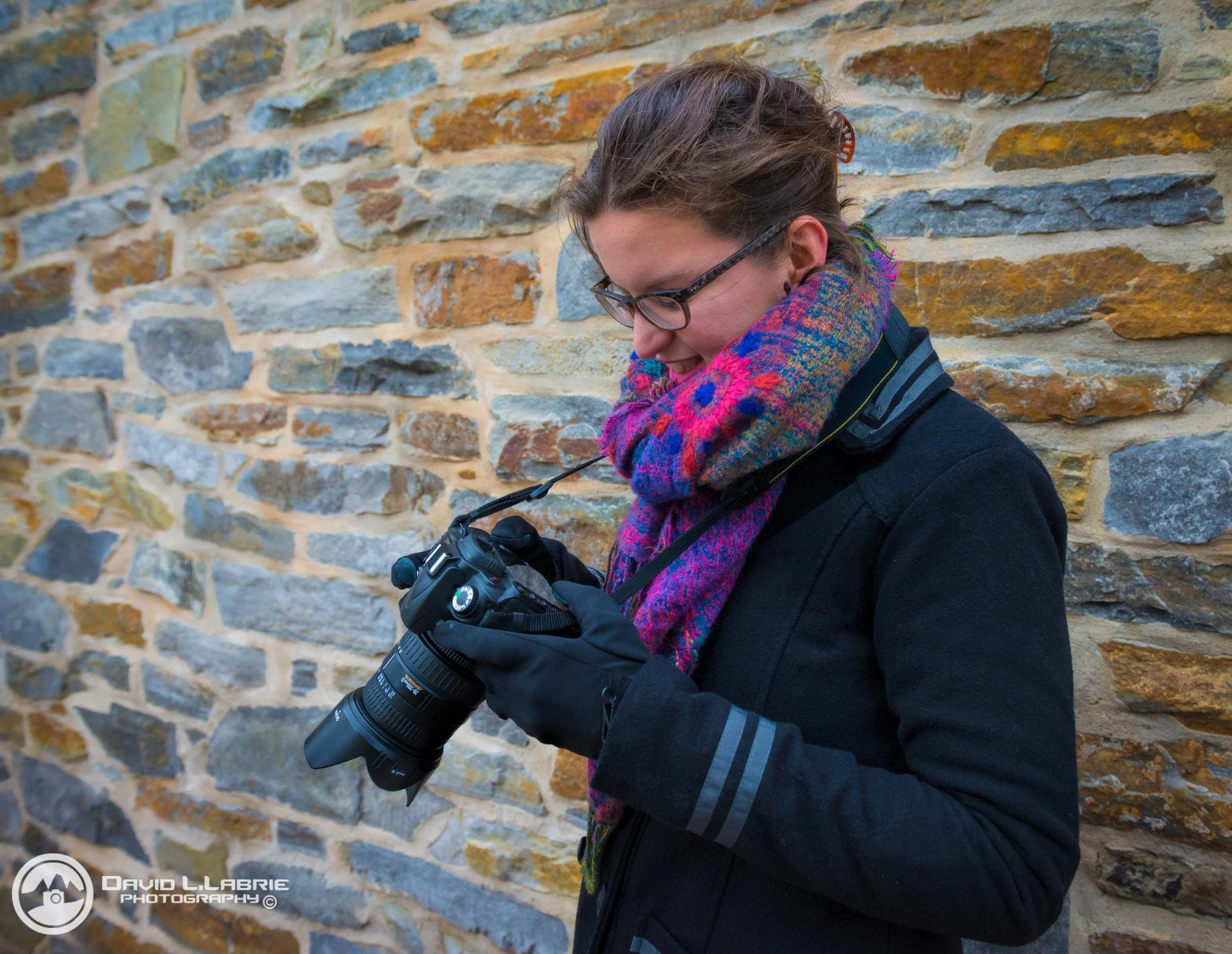 Woman looking at a digital camera while standing against a stone wall.