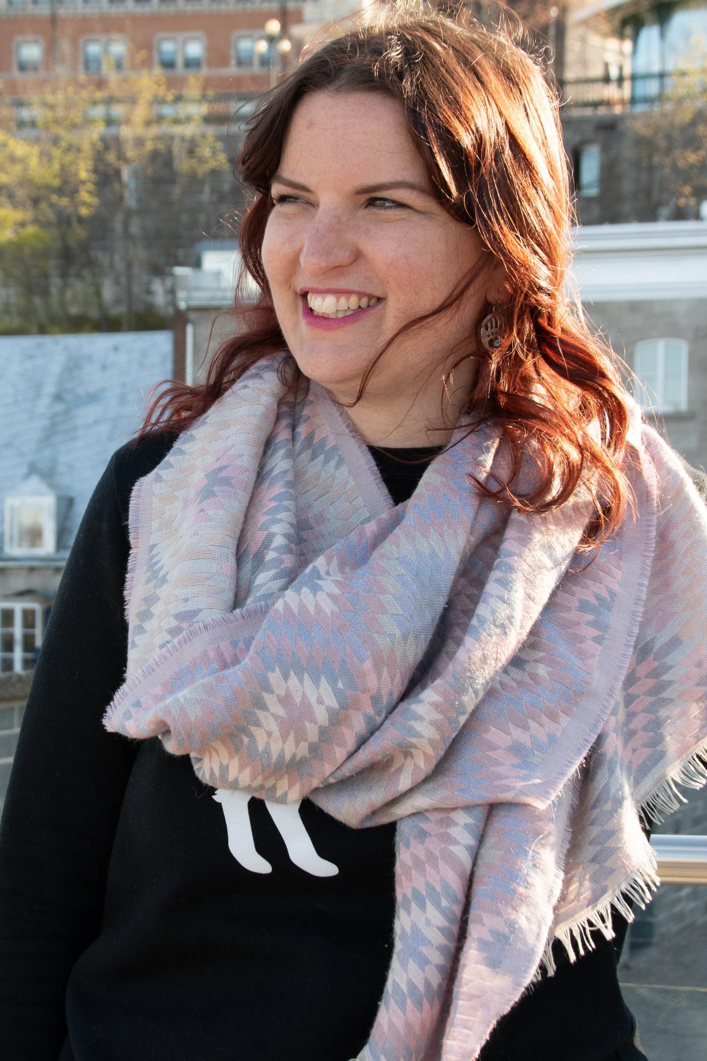Marie, a guide from Quebec, wearing a colorful scarf and a black top, stands outside with a building in the background on a sunny day.