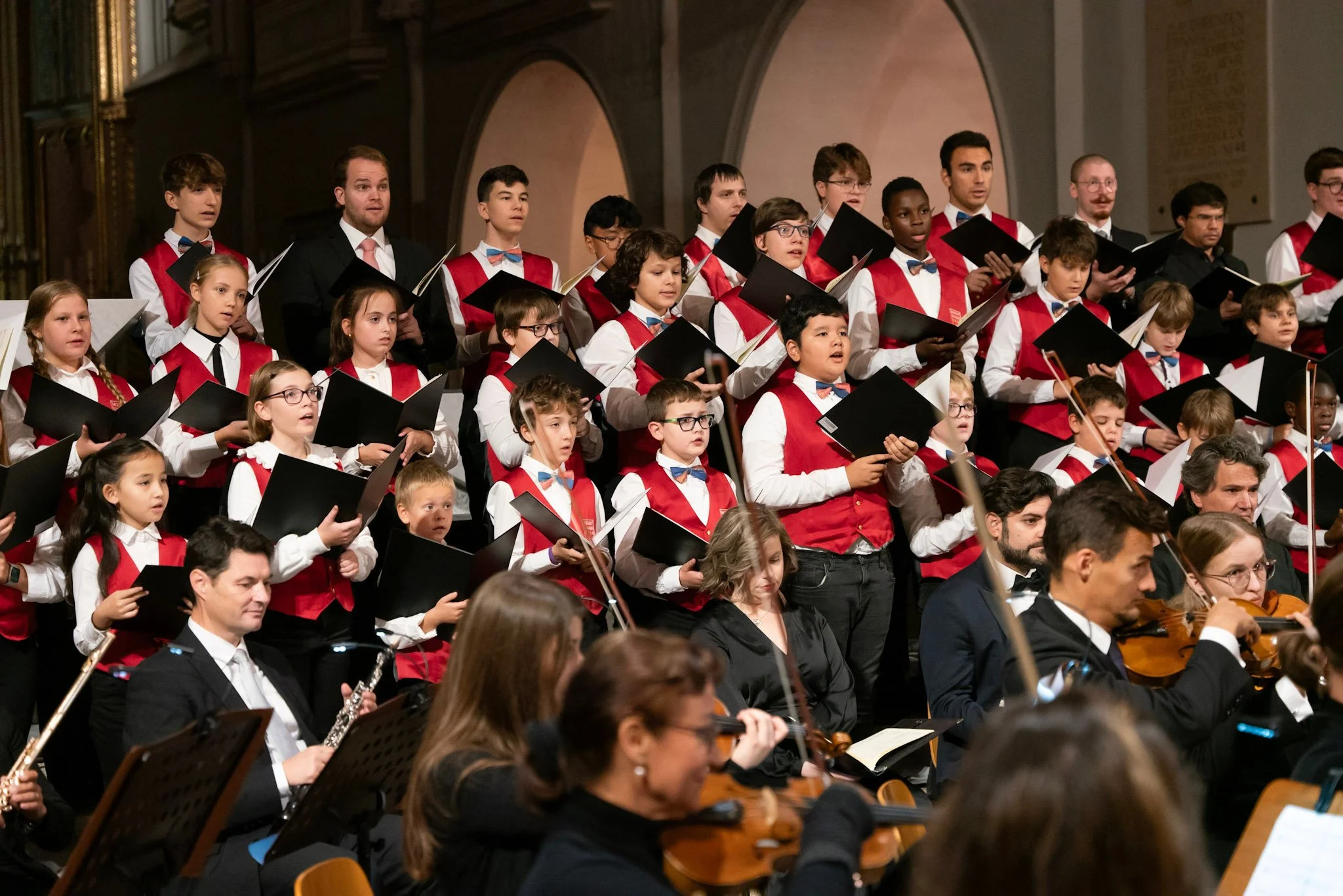 Junge Chorknaben und Erwachsene mit Orchester in einer Kirche während eines Konzerts.