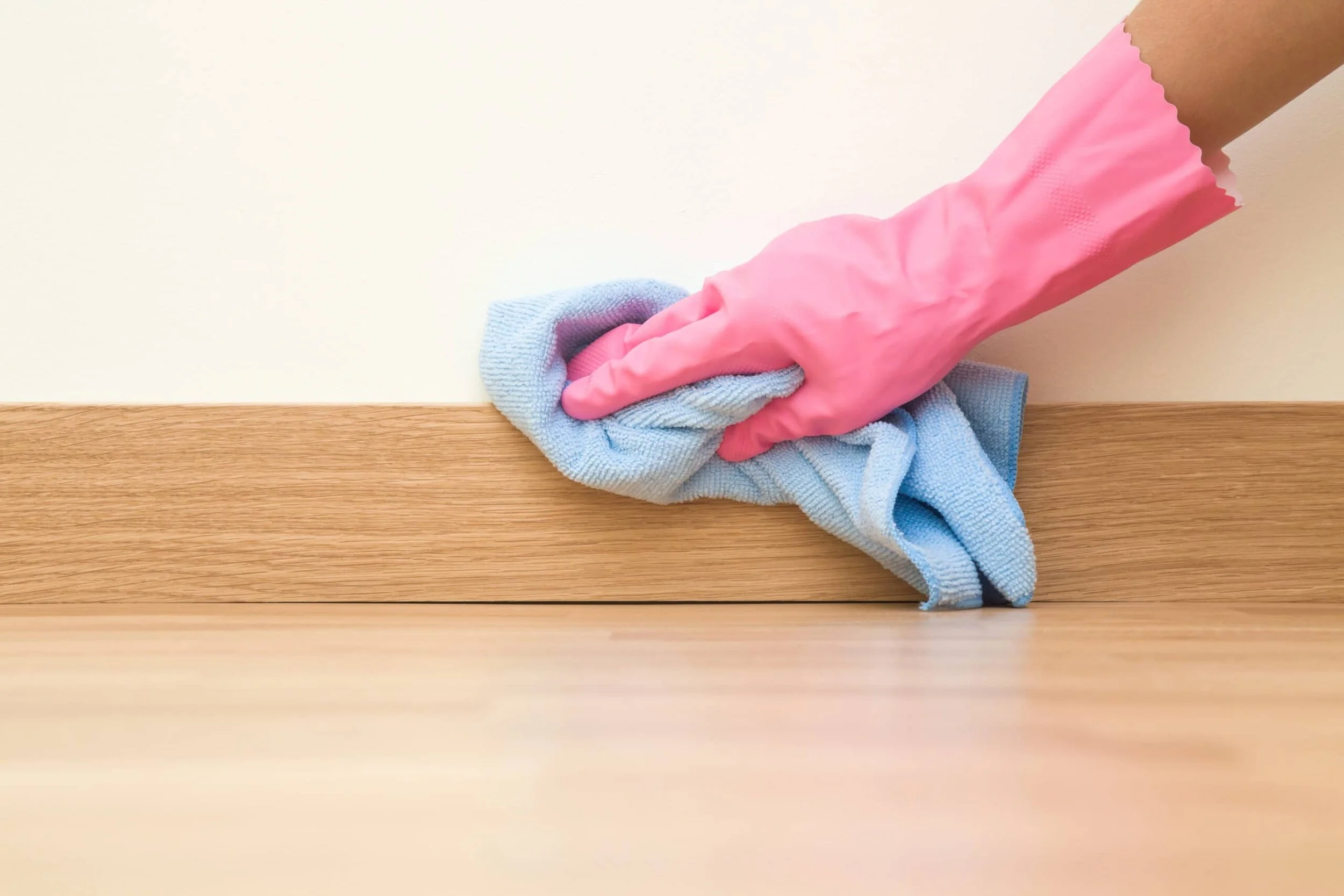Person wearing pink rubber glove cleaning a wooden surface with a blue cloth.