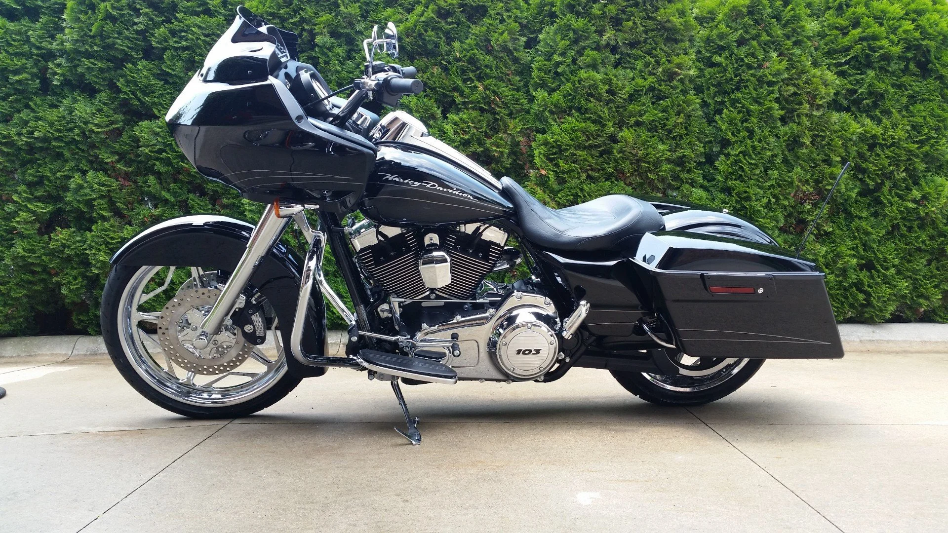 A black Harley-Davidson motorcycle parked on a concrete surface with green shrubbery in the background.