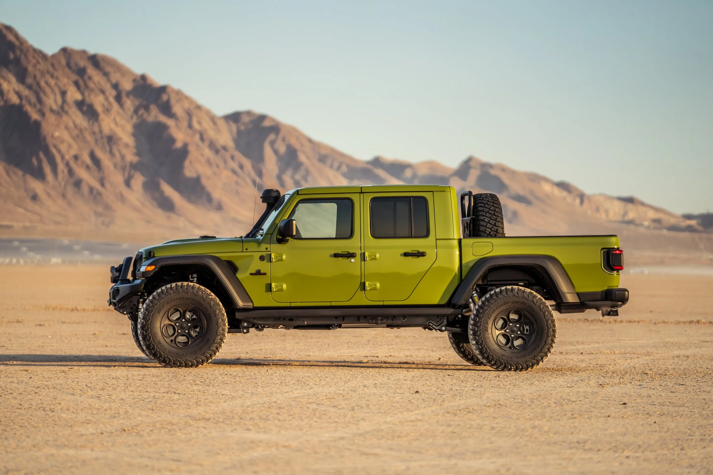 Green off-road pickup truck parked on a desert landscape with mountains in the background.