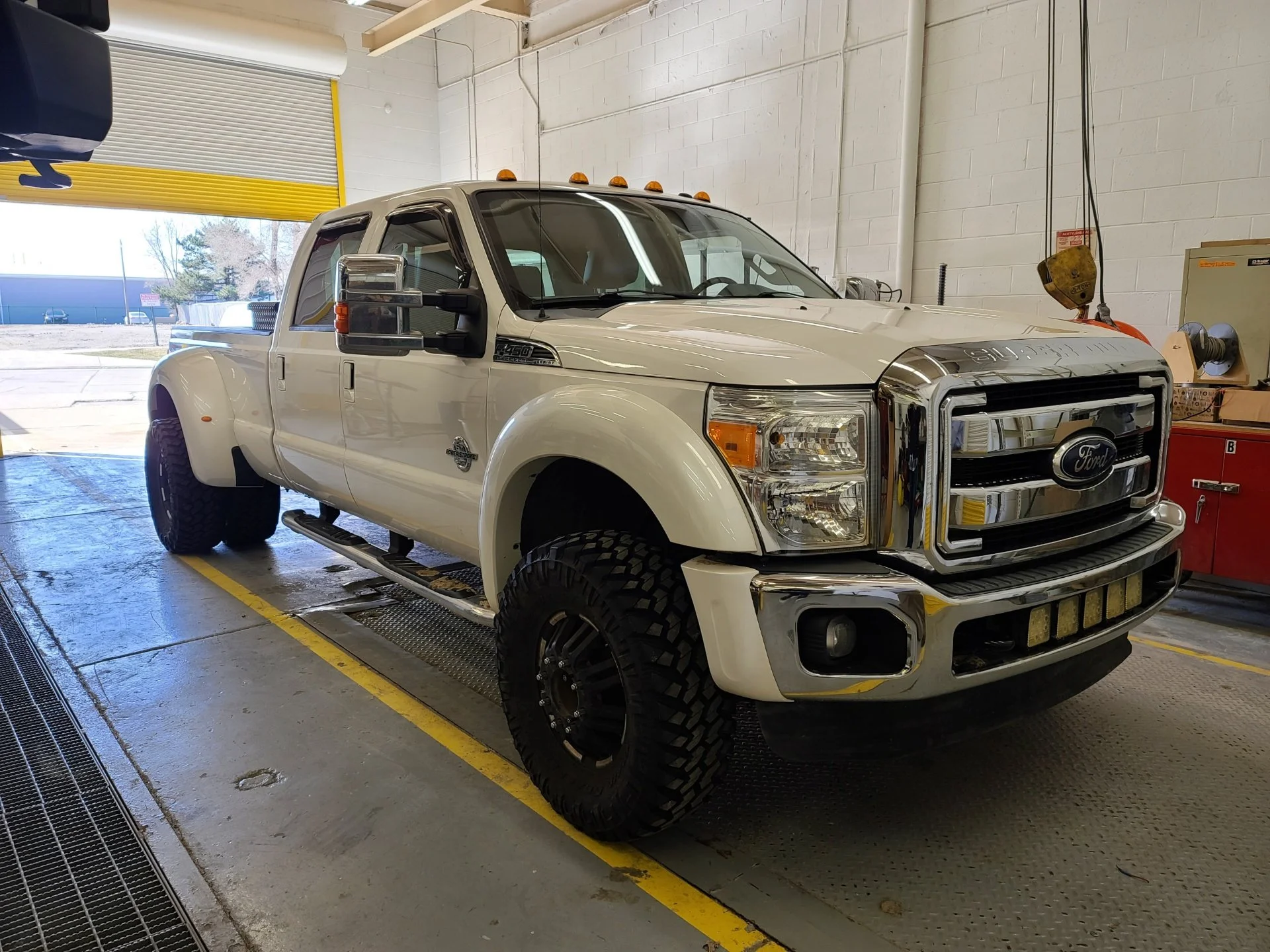 White Ford F-250 pickup truck inside a garage, with a large open door showing outdoors.