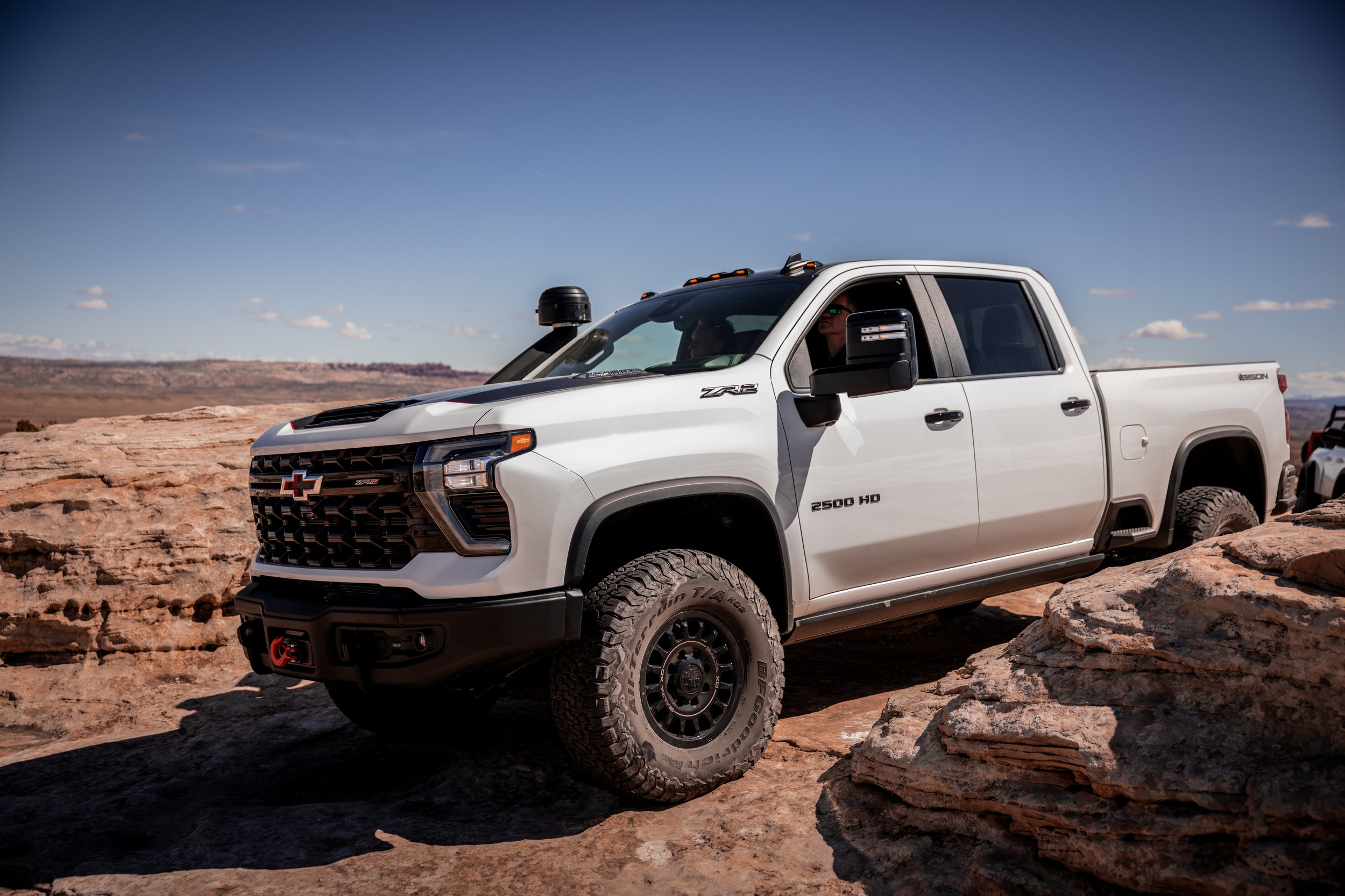 White Chevrolet Silverado 2500 HD off-road truck on rocky terrain, desert landscape, clear blue sky