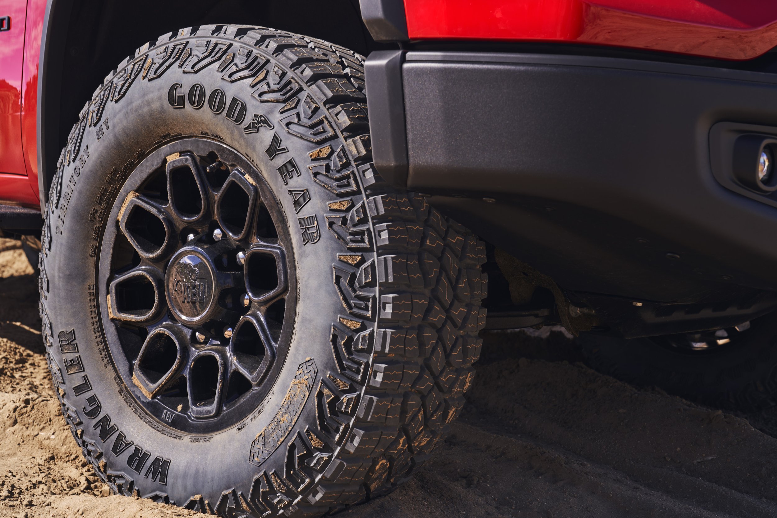 Close-up of a Goodyear Wrangler tire on a red off-road vehicle on a sandy terrain.