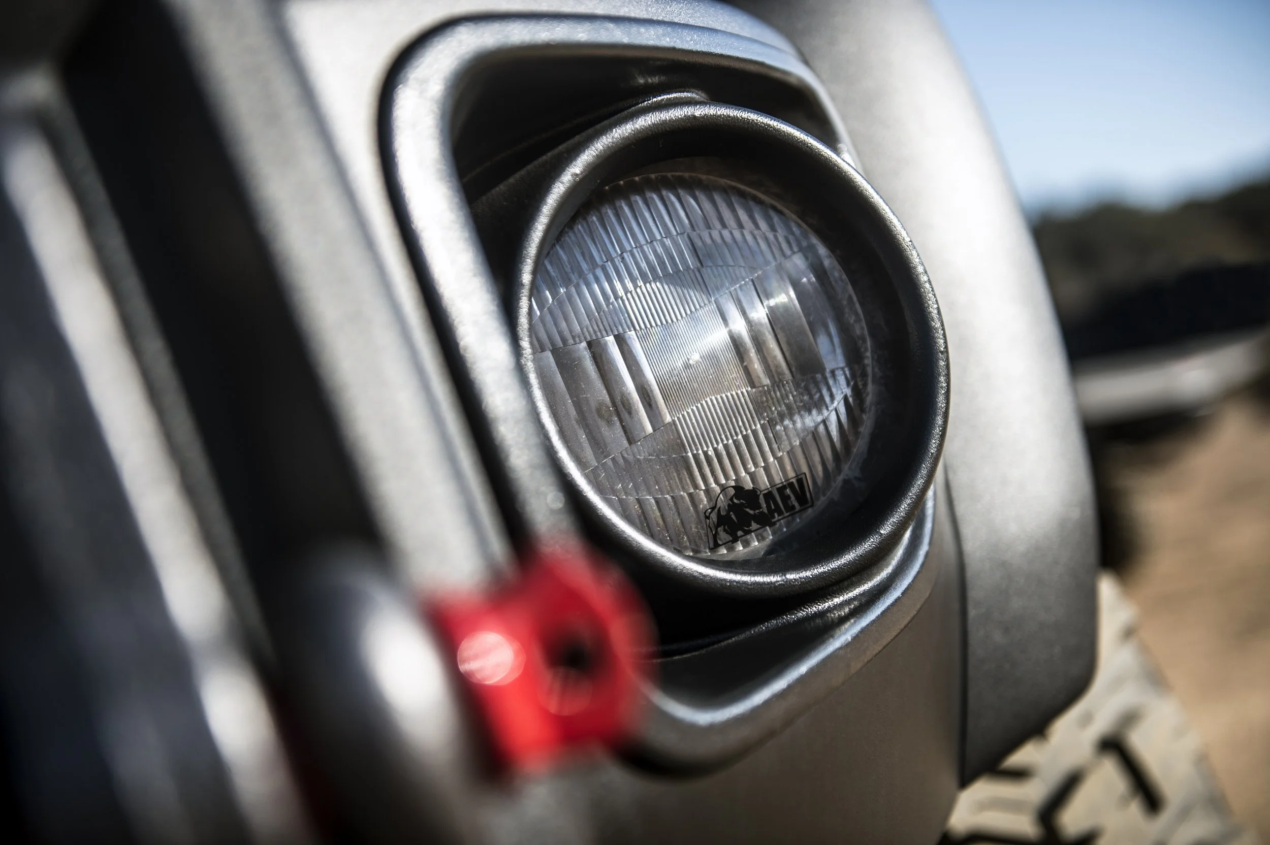 Close-up of off-road vehicle's round headlight with protective bezel and red screw behind it, outdoors setting.