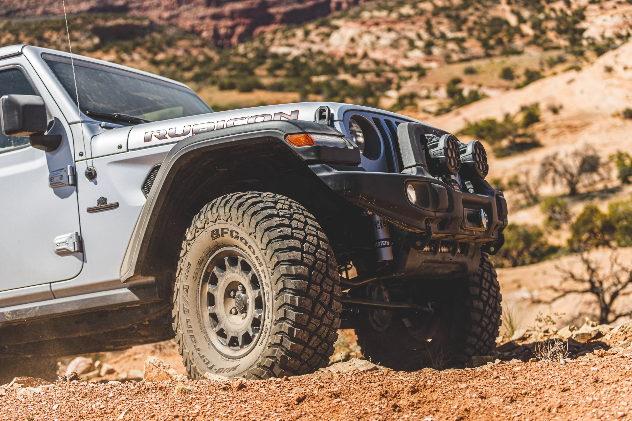 A white off-road Jeep Rubicon driving on rocky terrain in a desert landscape