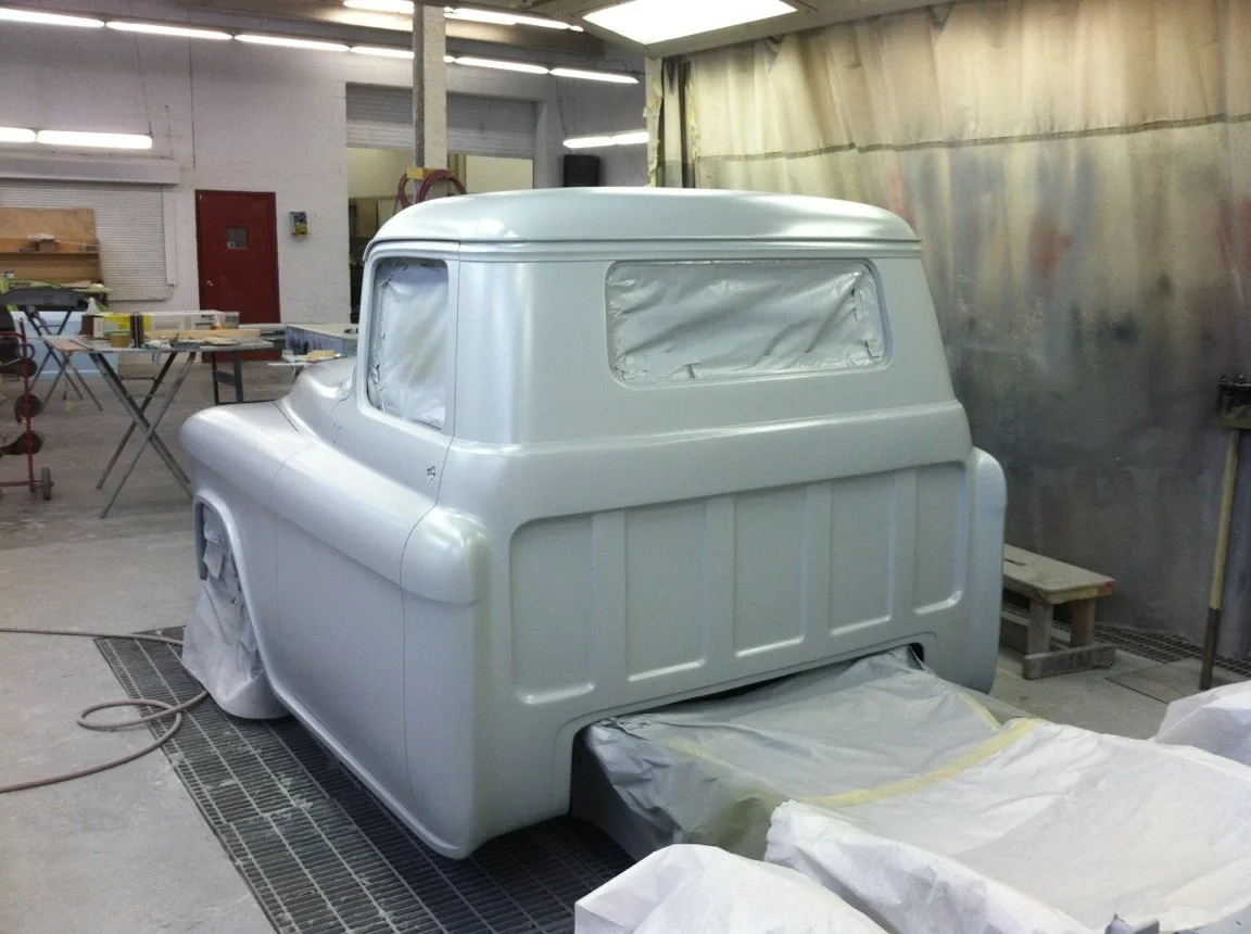 A vintage truck cab being painted white in an auto body shop.