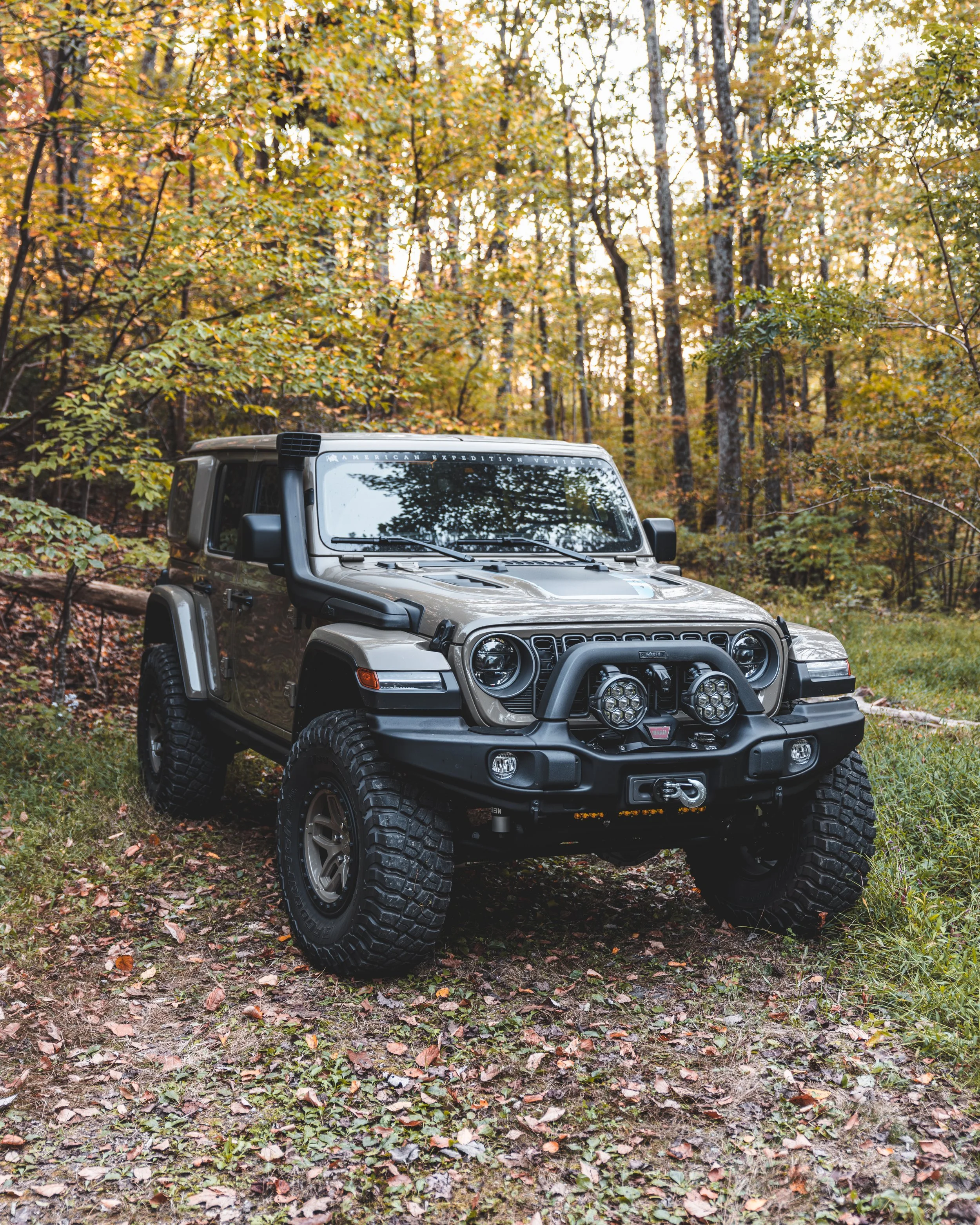 A rugged four-wheel-drive vehicle parked on a forest trail during autumn with trees and colorful leaves in the background.