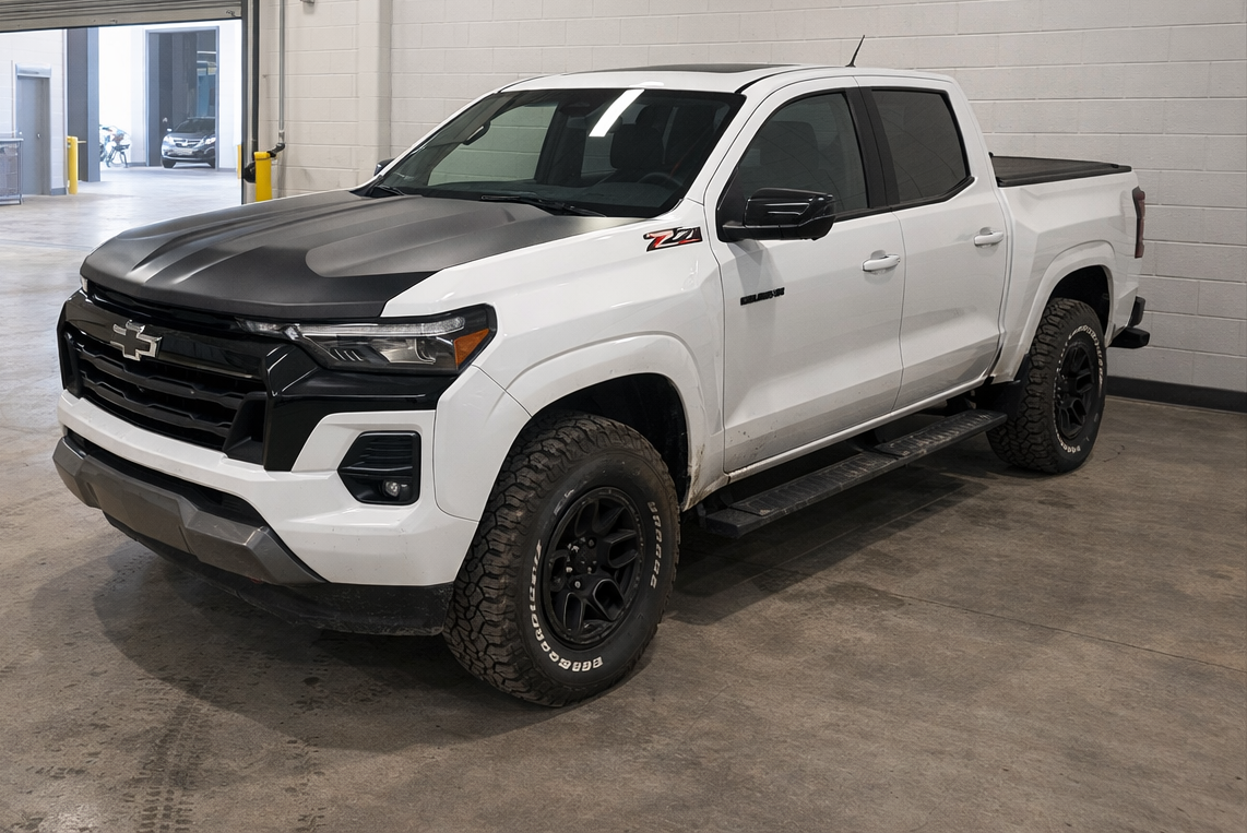 A white Chevrolet pickup truck parked indoors, featuring a black hood and black accents, with off-road tires and a Z71 badge on the side.