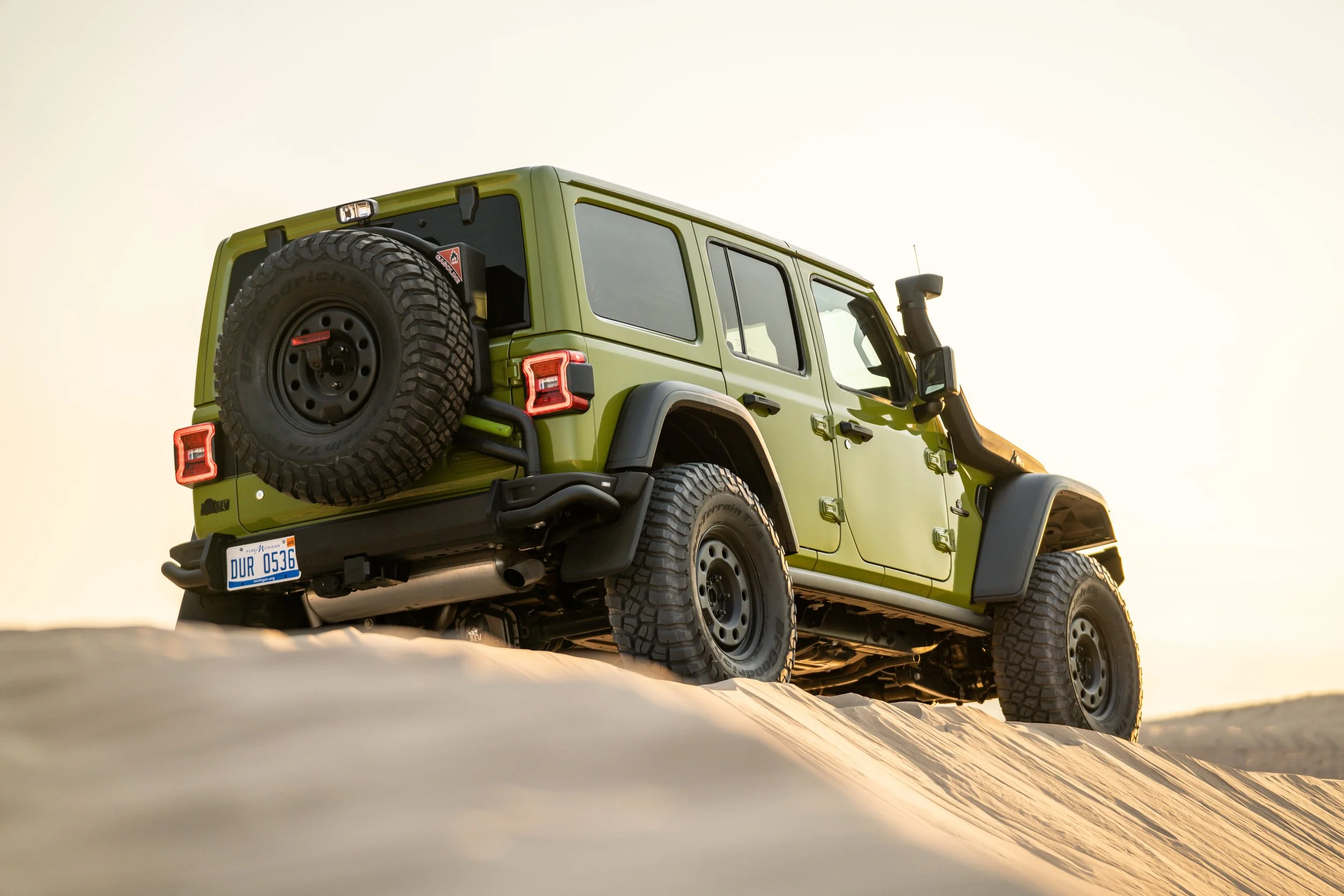 Green off-road SUV driving on sandy terrain during sunset.