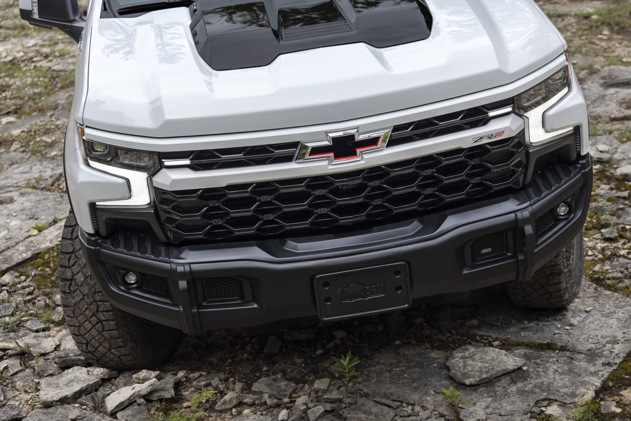 Front view of a white Chevrolet pickup truck with a black grille and a Chevrolet emblem, parked on a rocky surface.