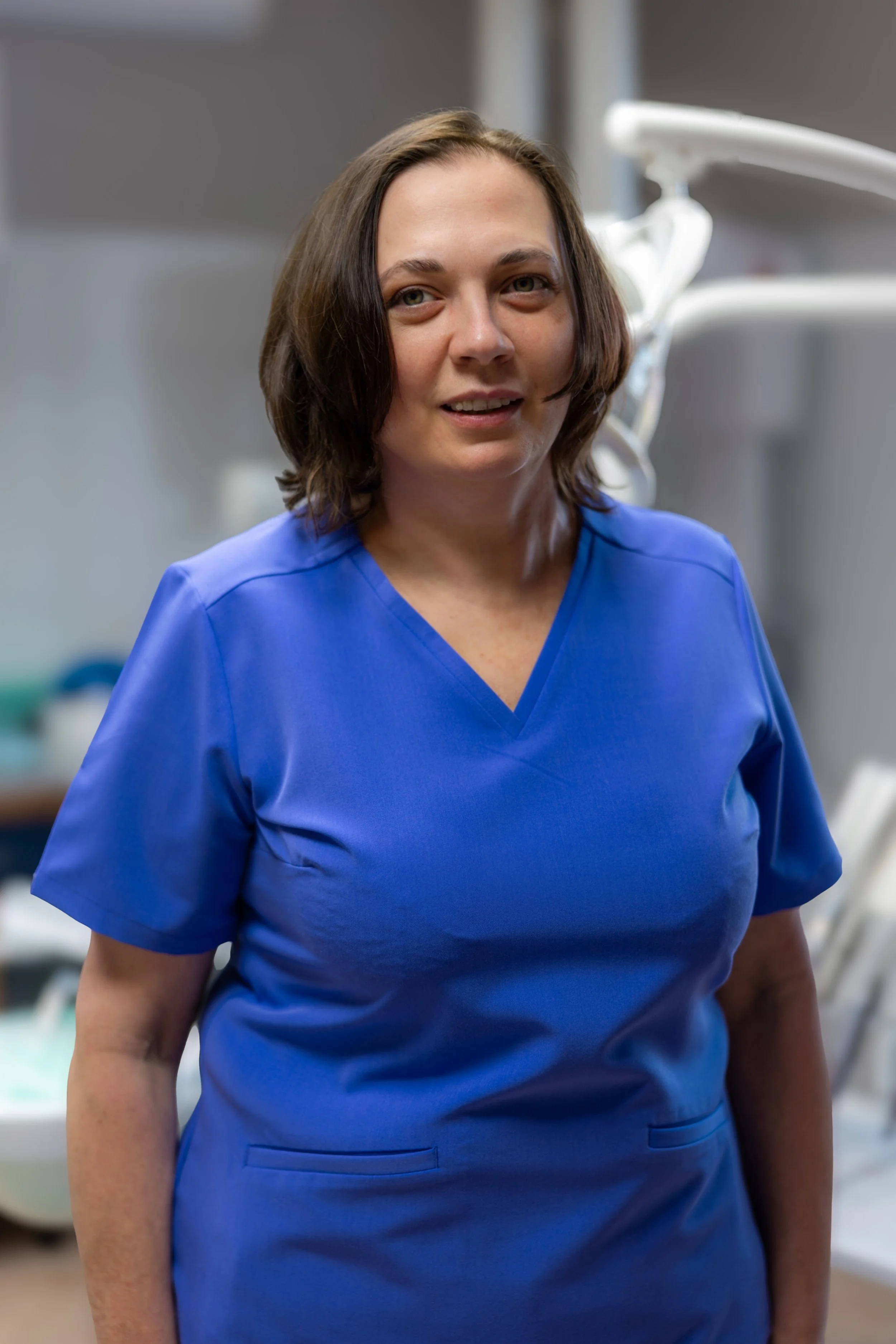 A woman in blue scrubs standing in a medical or dental office.