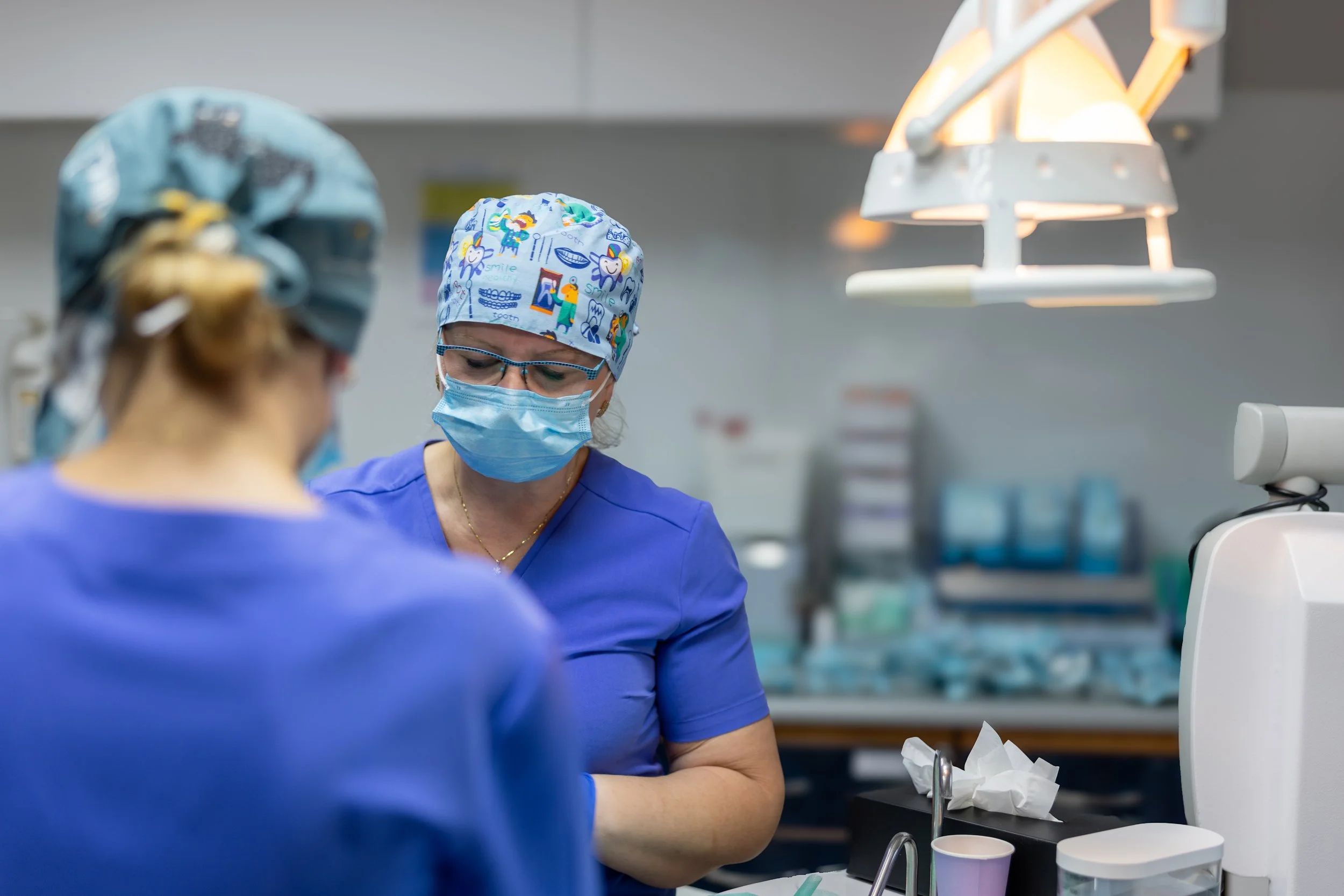 Two medical professionals in scrubs and masks working in a hospital operating room.