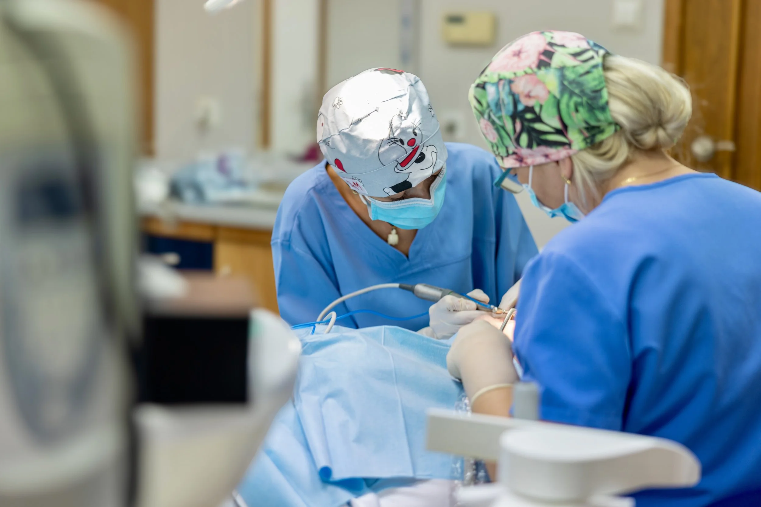 Two medical professionals in scrubs and masks performing a procedure in an operating room.