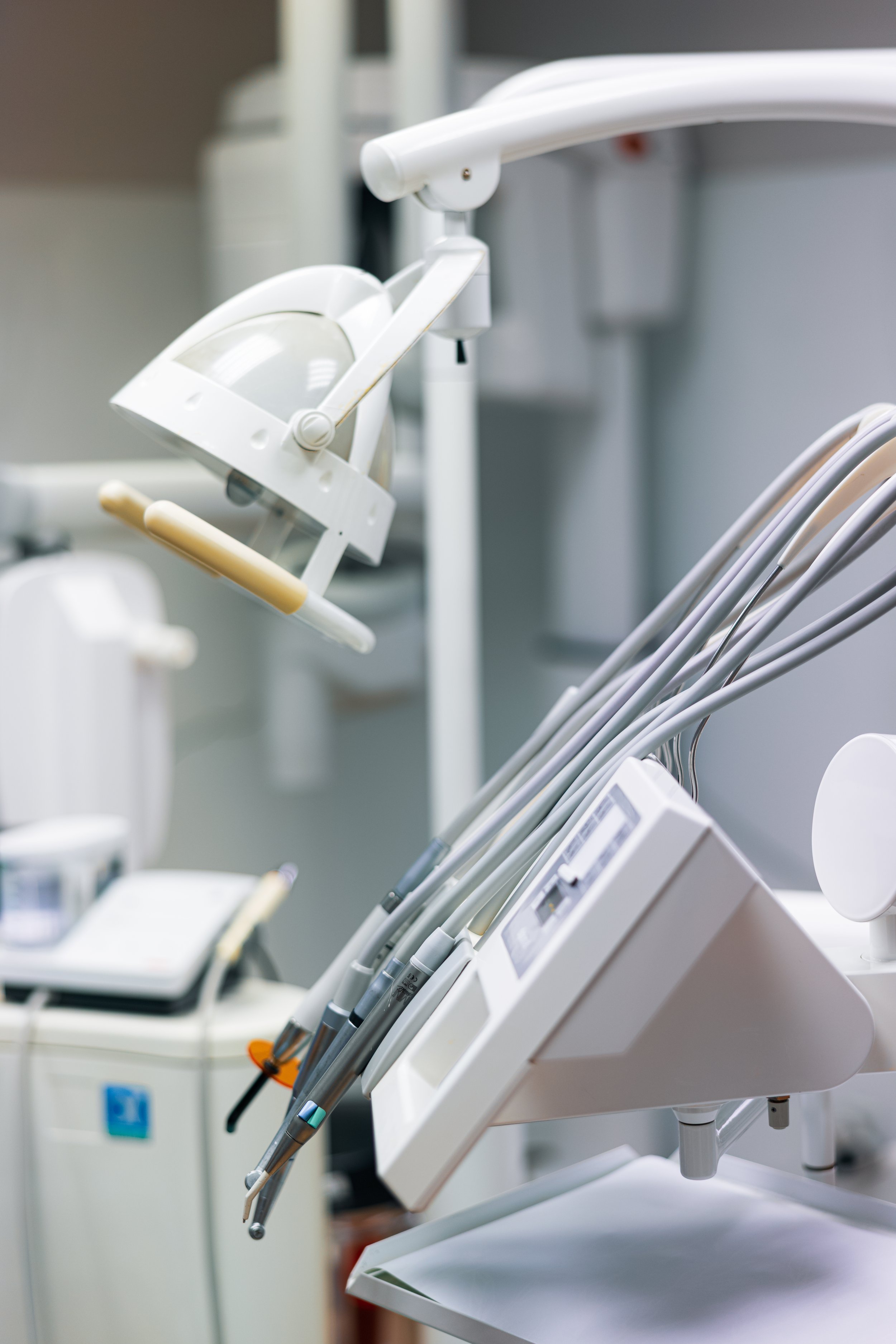Dental clinic equipment including a dental lamp, handpieces, and other dental tools on a trolley in a clinical setting.